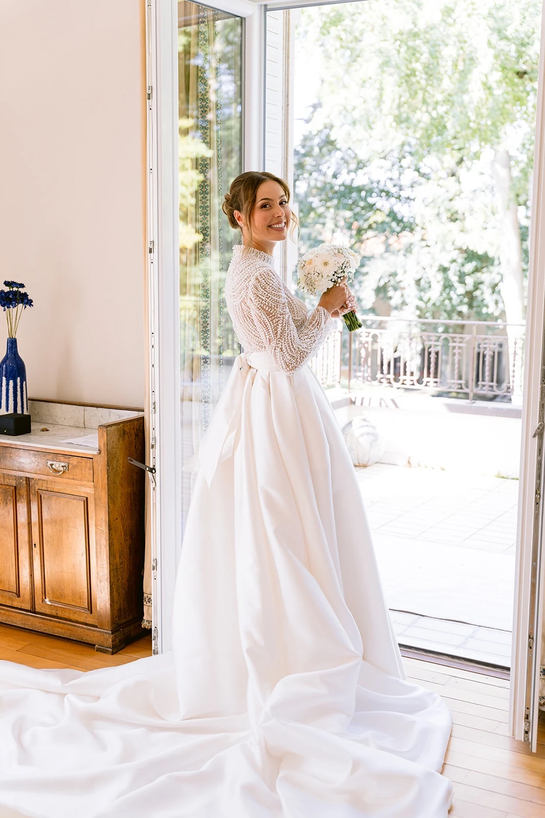 La mariée se retourne vers l’appareil devant une porte donnant sur le jardin.