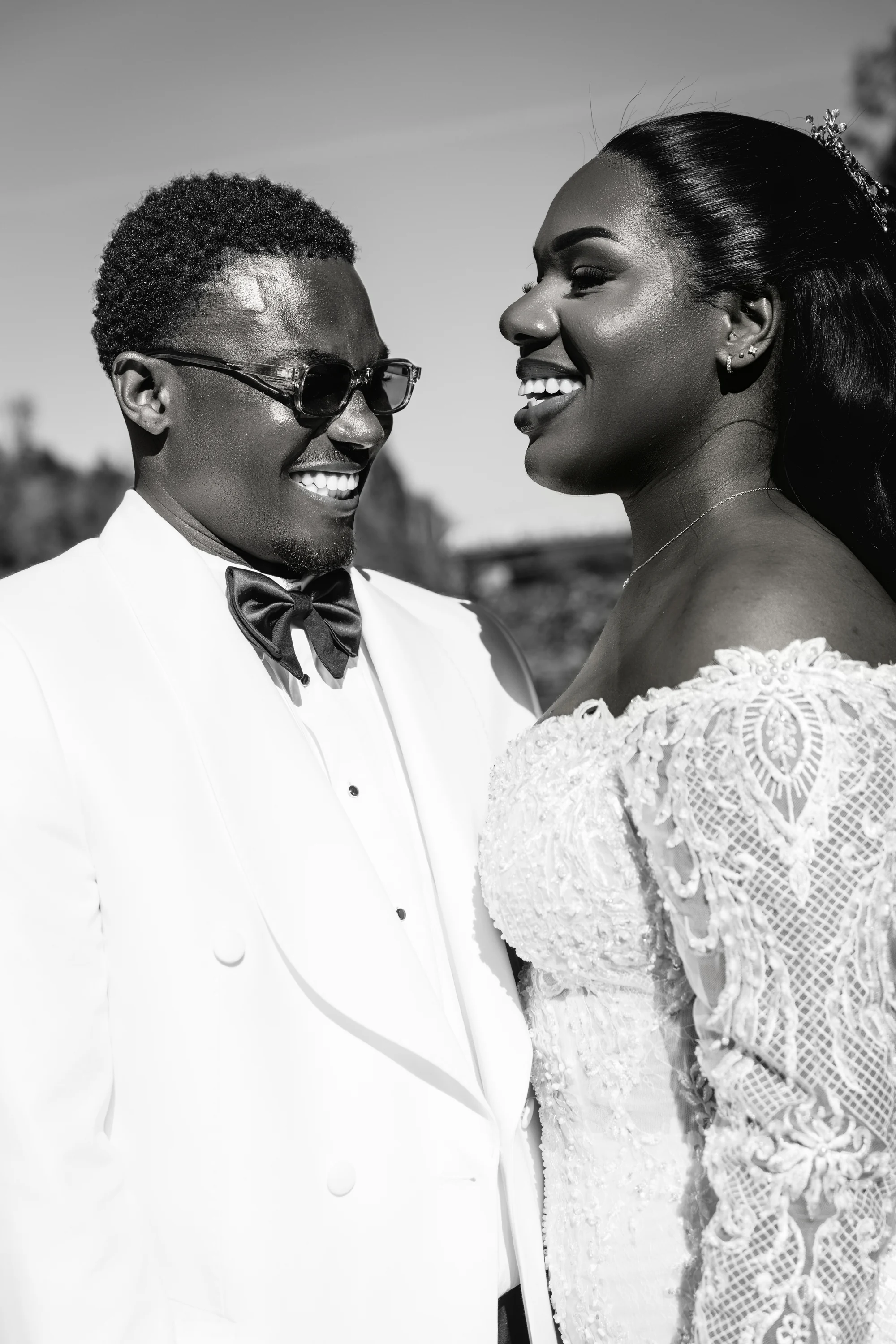 Les mariés échangent un sourire en lumière naturelle, en noir et blanc.
