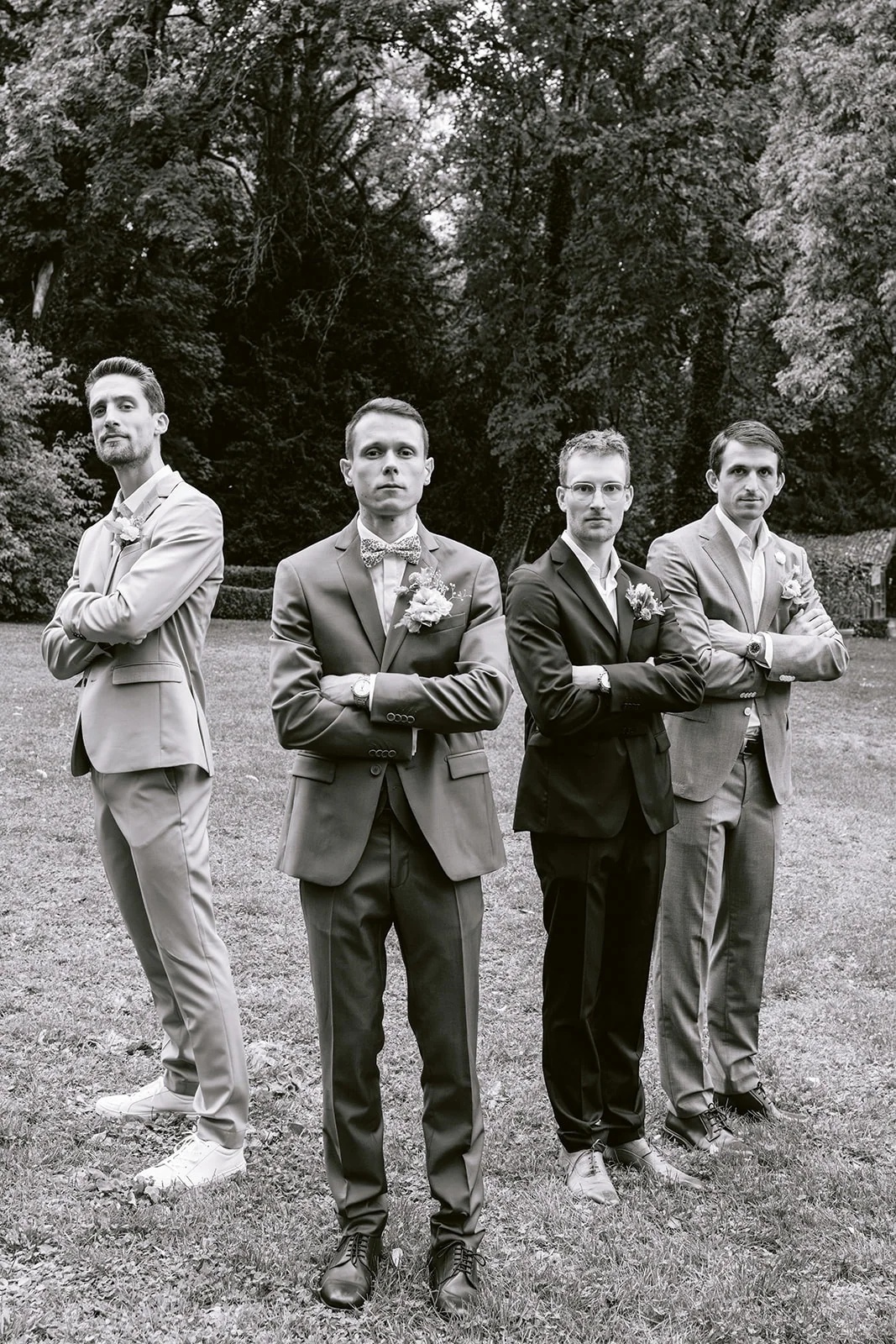 En noir et blanc, quatre hommes en costume posent les bras croisés dans le jardin.