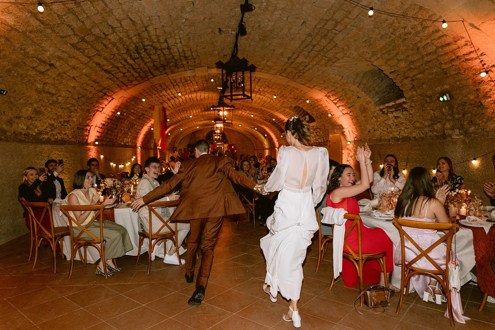 Vus de dos, les mariés dansent entre les tables de réception devant les invités qui applaudissent.
