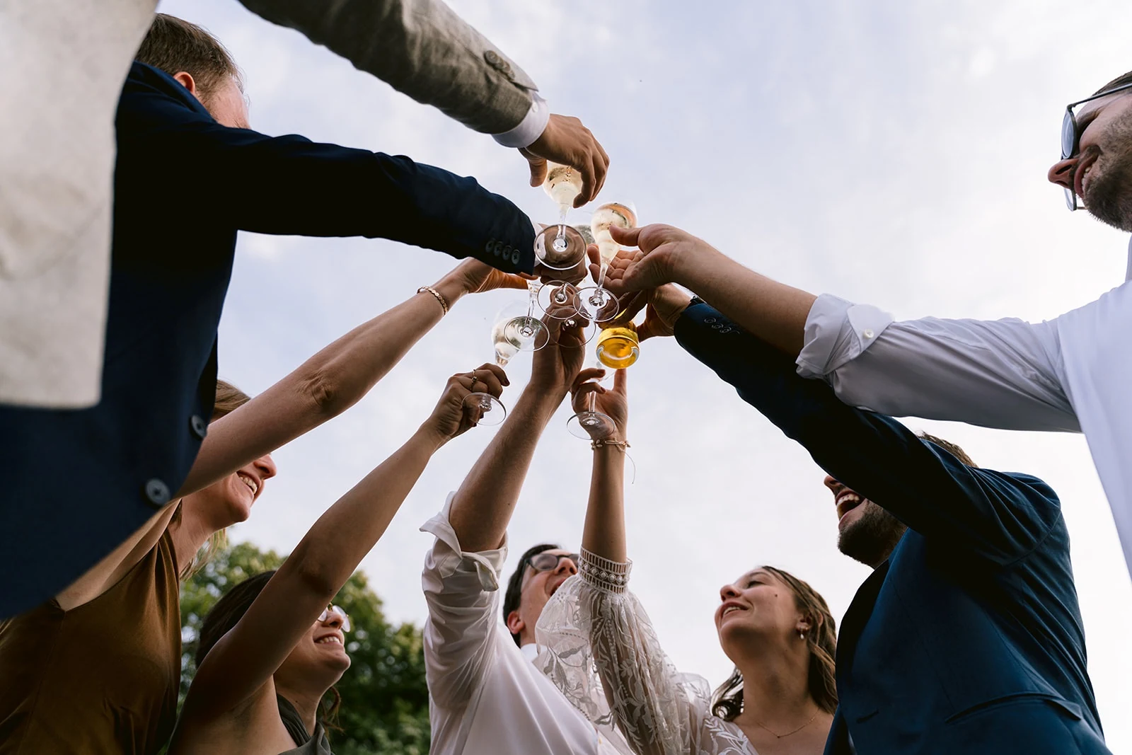 Photographiés en contre-plongée, les mariés et plusieurs invités lèvent leurs verres ensemble sous le ciel.