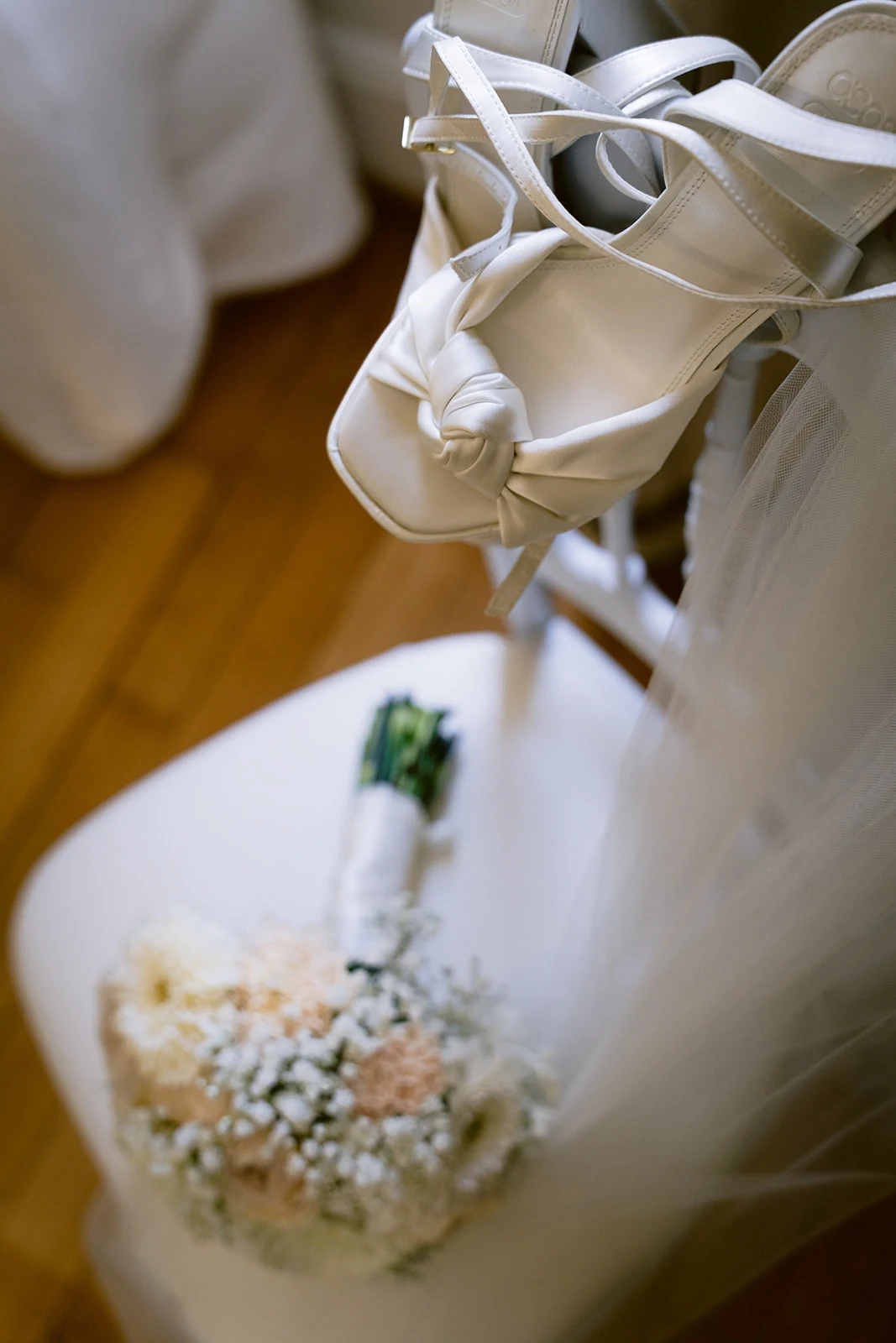 Des sandales blanches à talons sont disposées près d’une boutonnière fleurie.