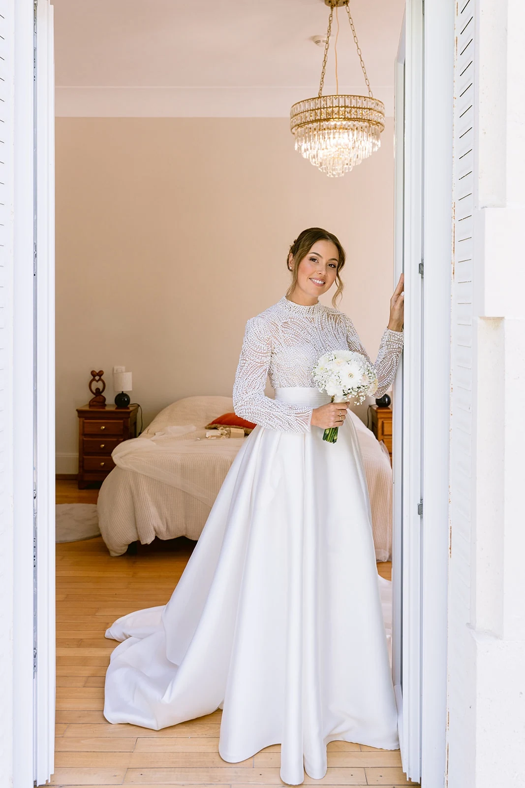 La mariée tient son bouquet dans l’encadrement de la porte de sa chambre.