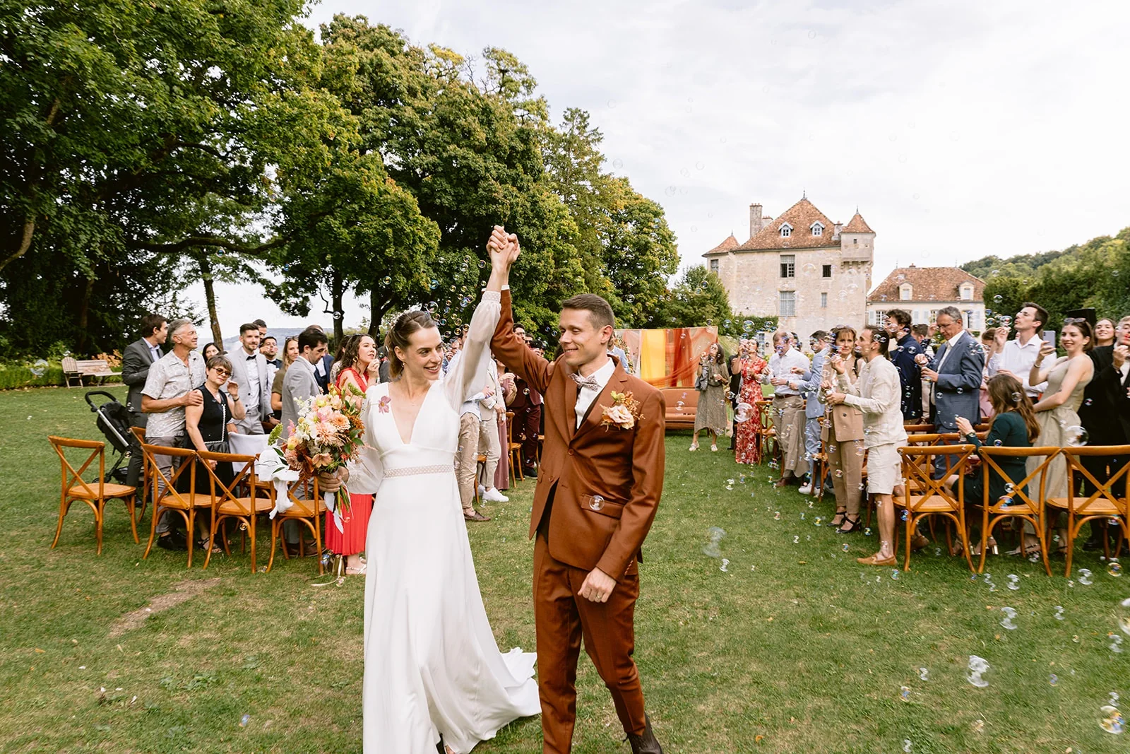 Les mariés lèvent leurs mains jointes en avançant entre les rangées d’invités.