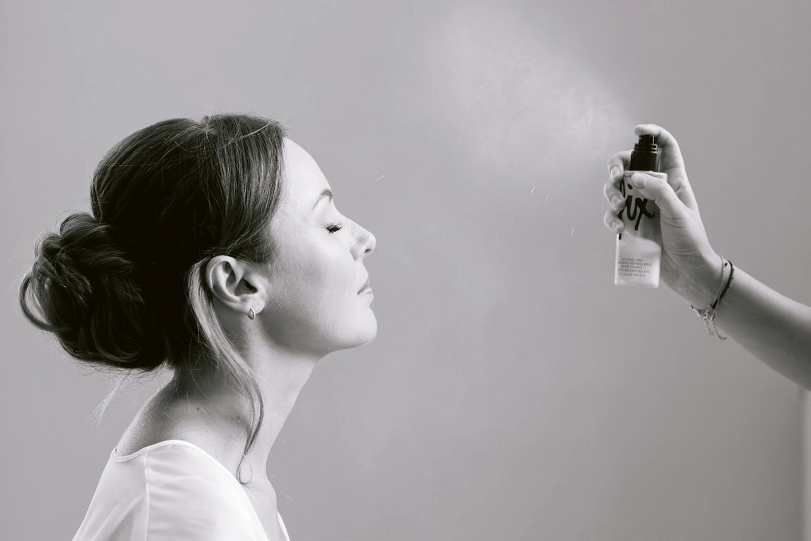 En noir et blanc, la mariée ferme les yeux pendant les dernières touches de maquillage.