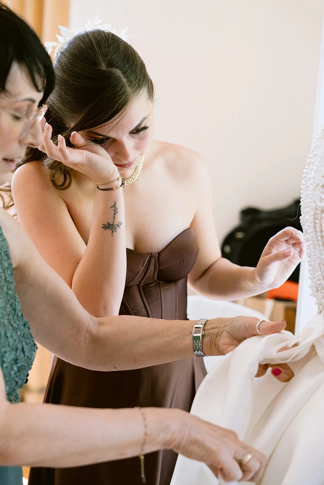 Les mains d’une proche ajustent les détails de la robe de mariée.