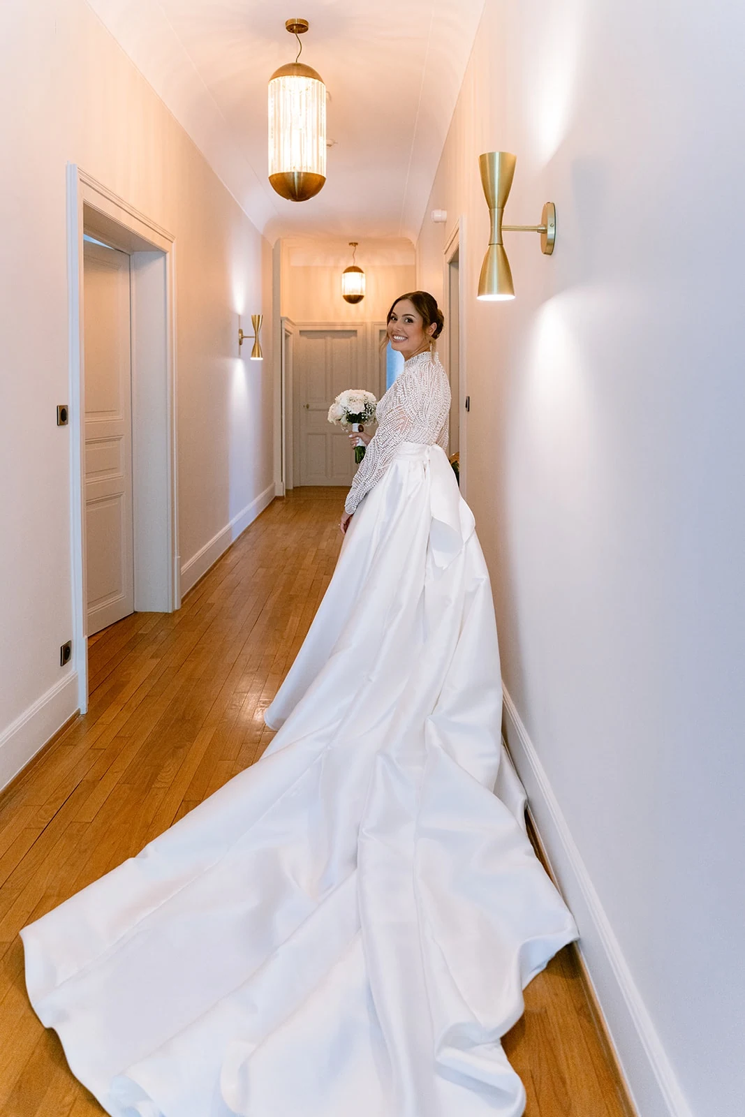 La longue traîne de la robe se déploie dans le couloir derrière la mariée.