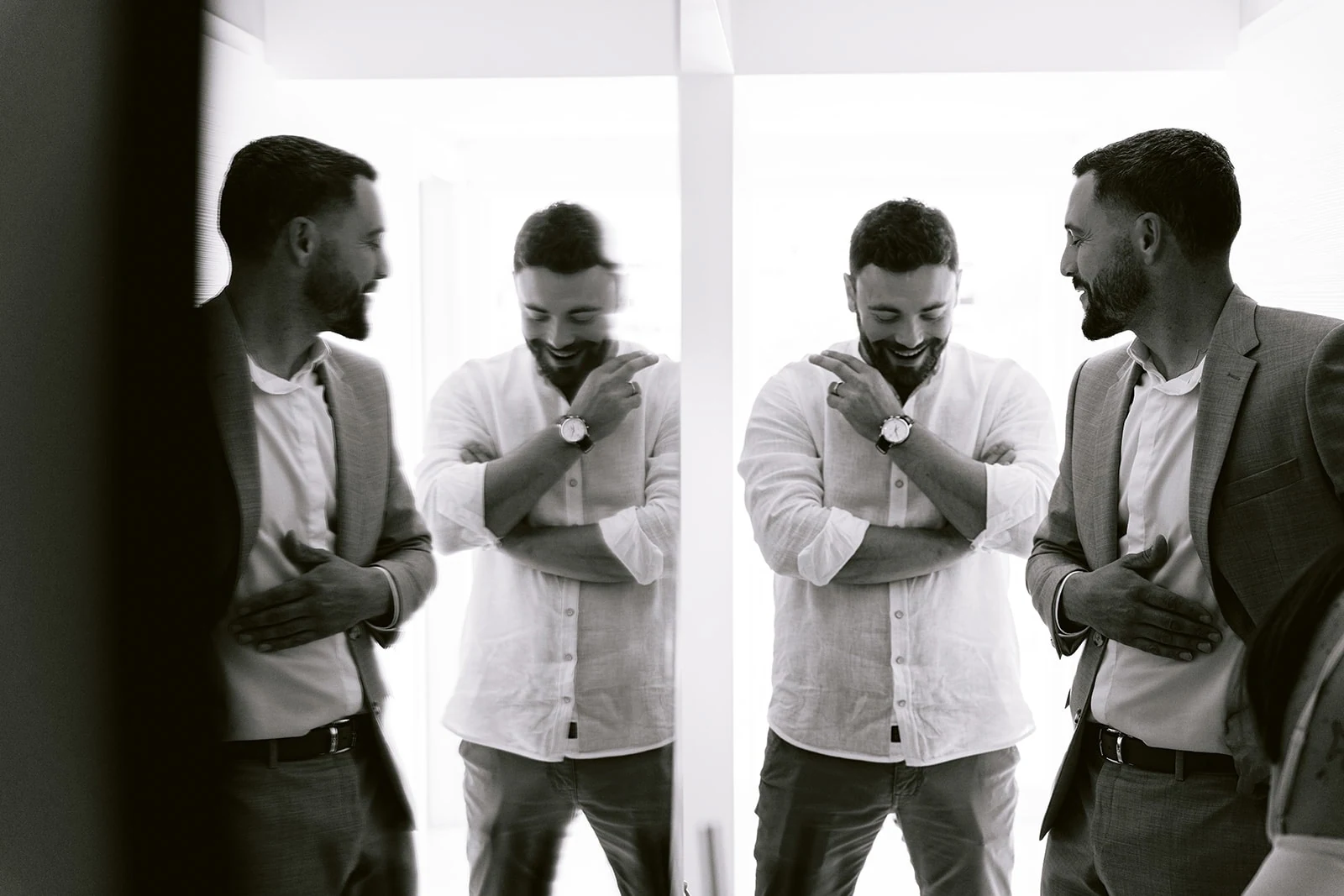 En noir et blanc, le marié partage un sourire avec deux proches pendant les préparatifs.