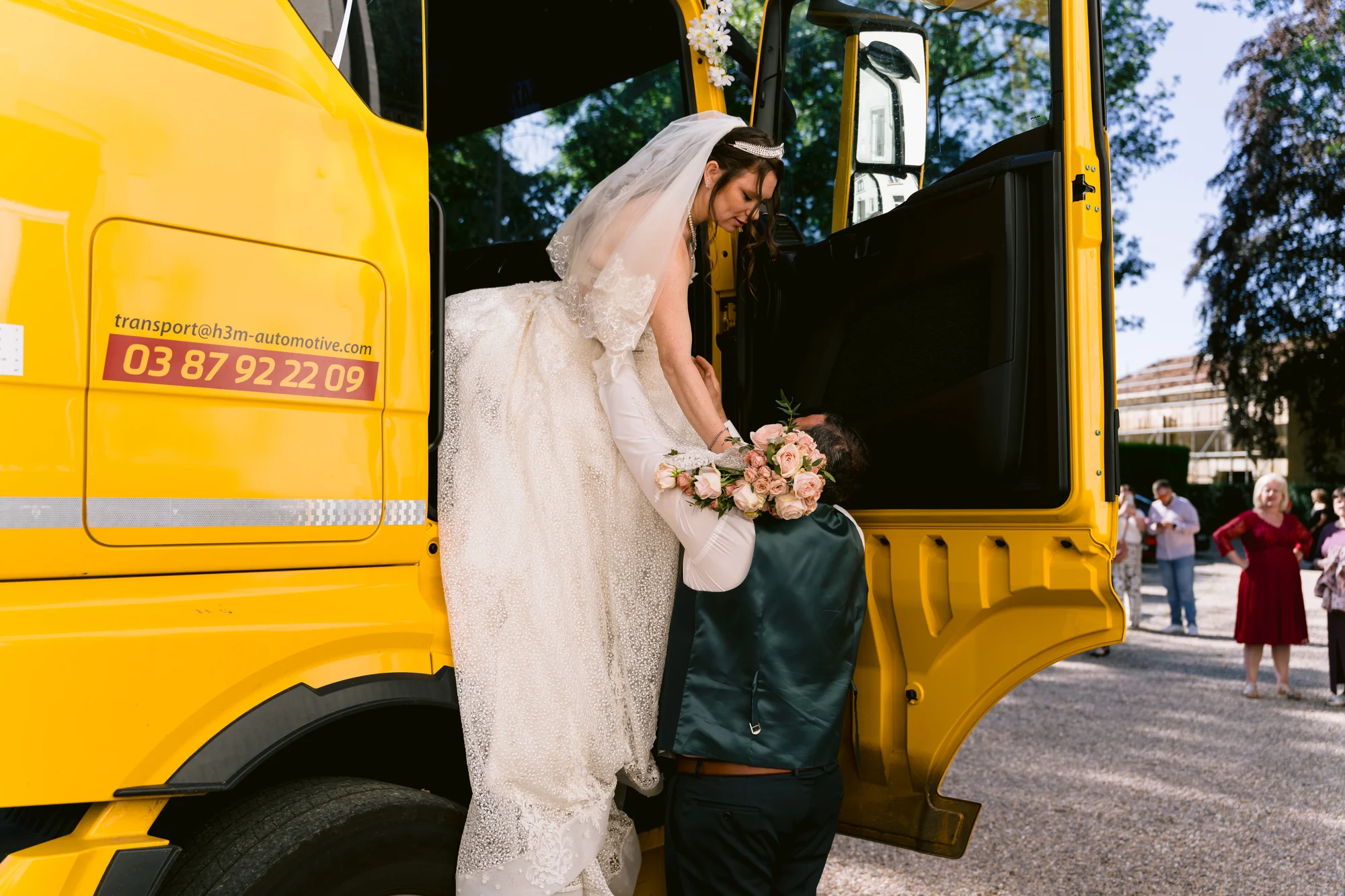 La mariée descend d’un autocar jaune, son bouquet à la main.