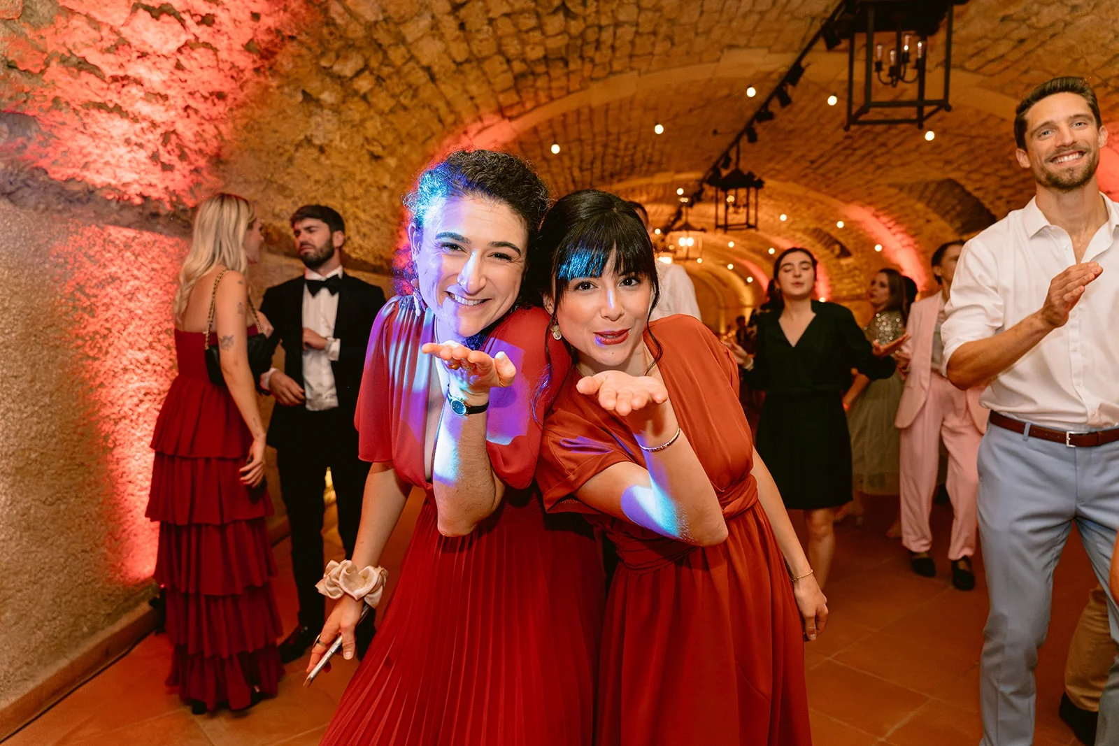 Deux femmes en robes rouges envoient des baisers vers l’objectif sur la piste de danse.