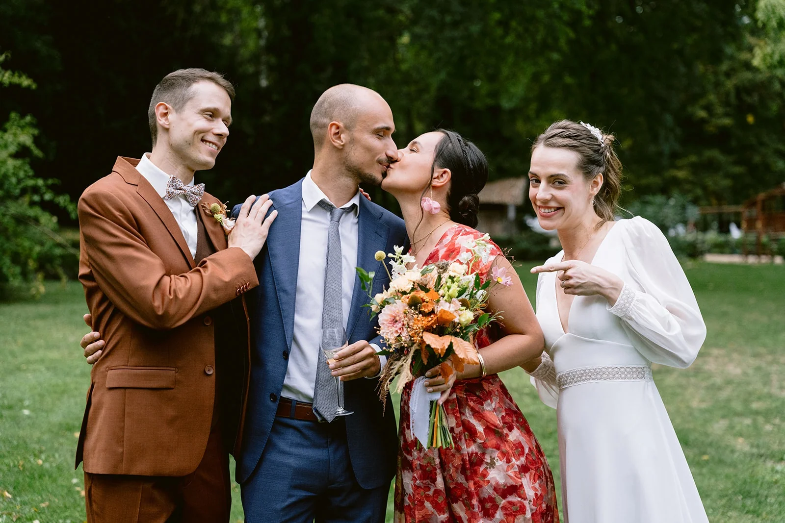 Les mariés sourient aux côtés de deux invités qui s’embrassent dans le jardin.