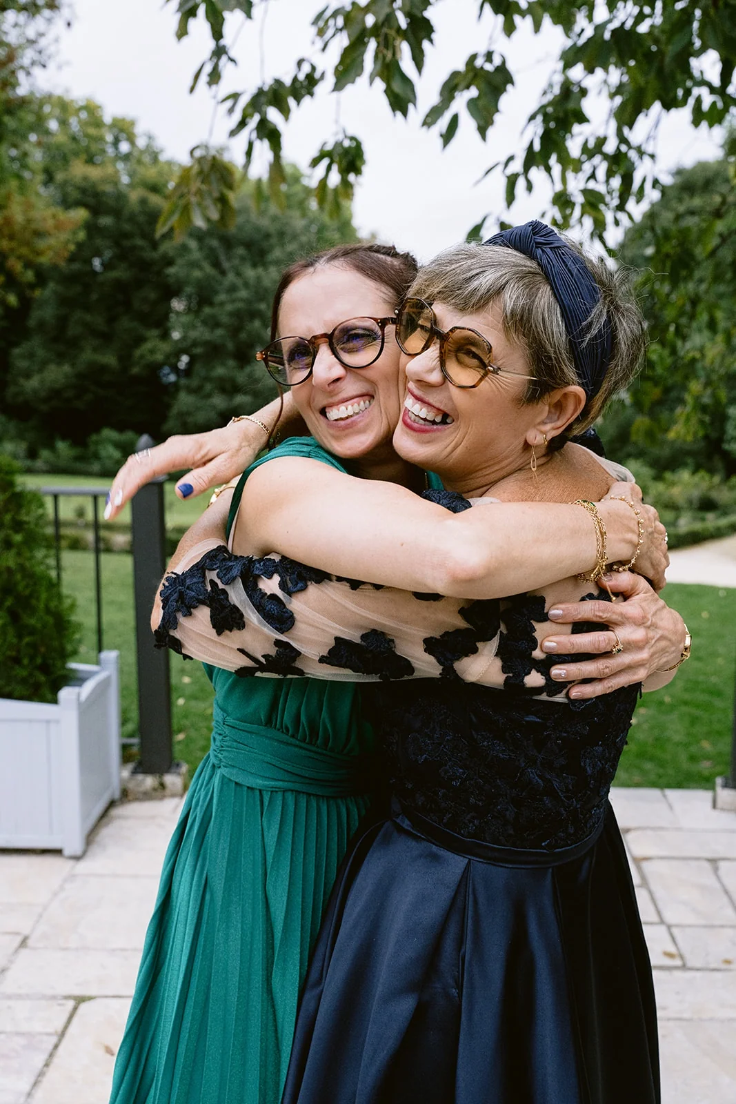 Deux femmes portant des lunettes se serrent dans les bras en riant, sur une terrasse.