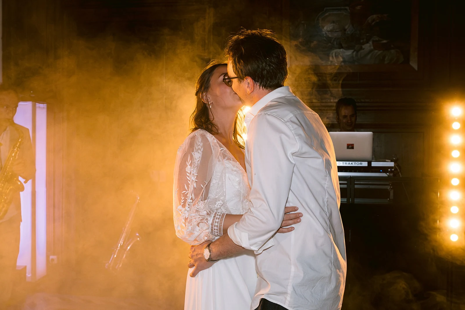 Les mariés s’embrassent sur la piste de danse, entourés d’une brume éclairée de lumière dorée.