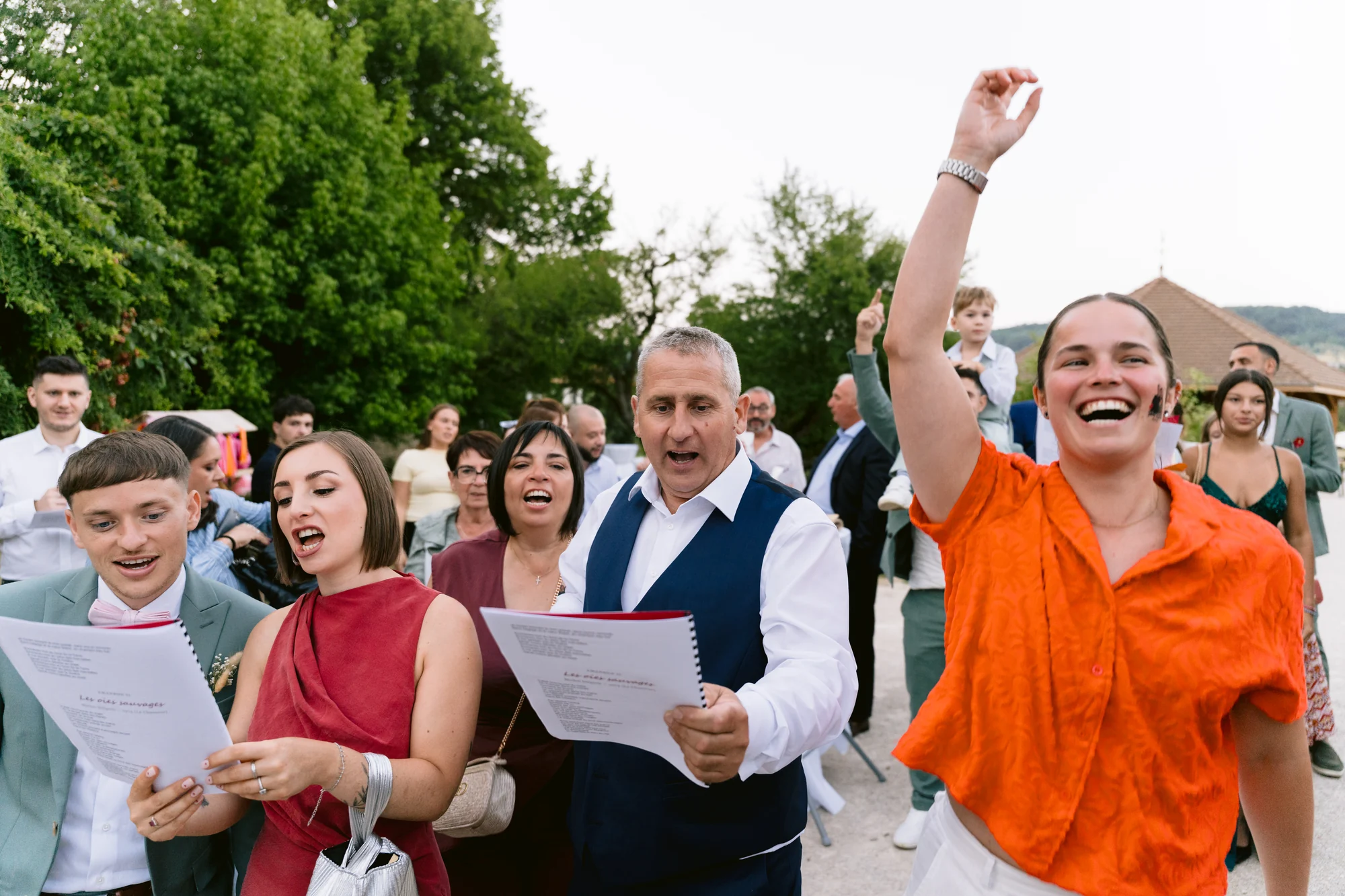 Des invités chantent en riant, une jeune femme lève le bras.
