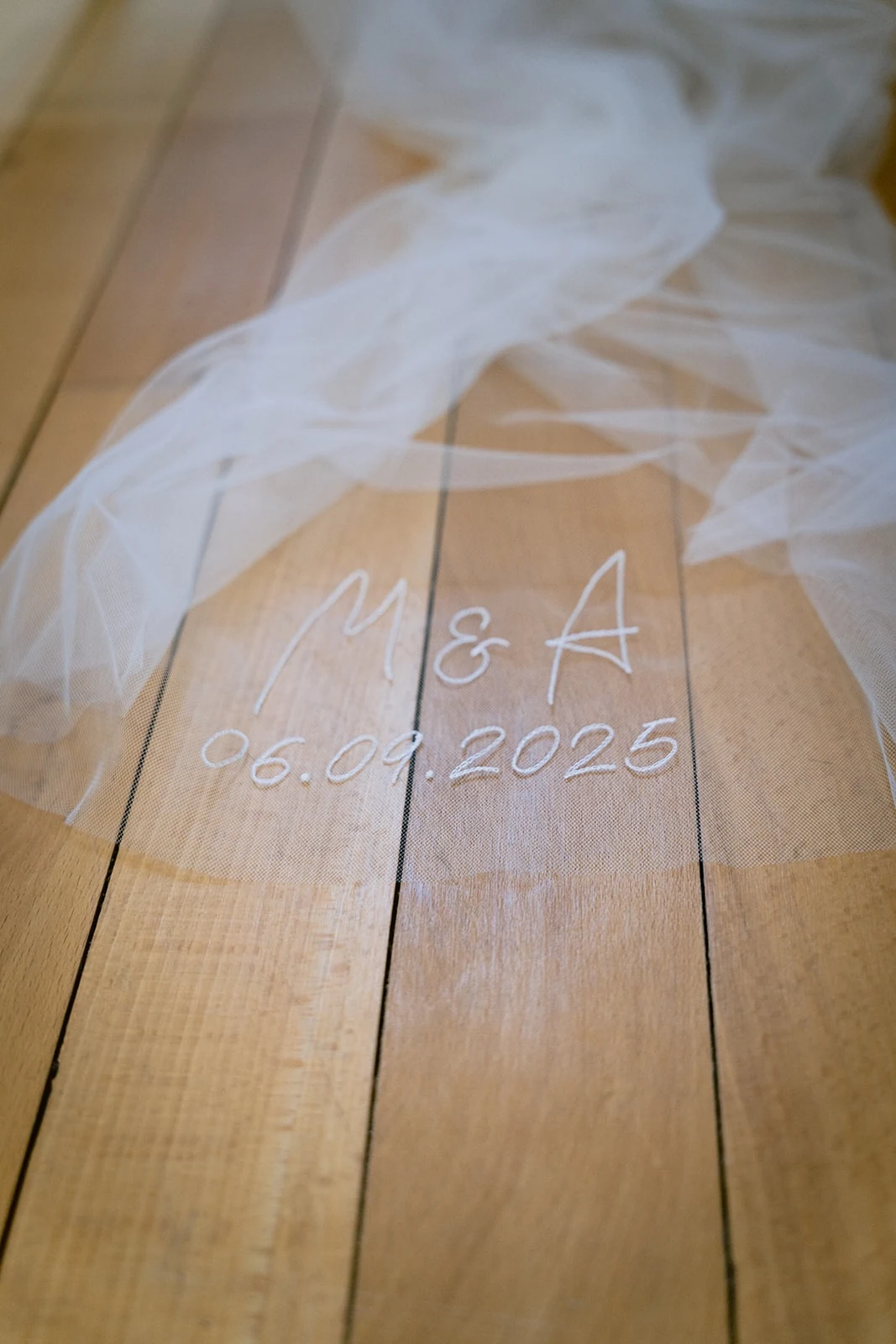 Détail du voile brodé d’initiales et d’une date, posé sur le parquet.