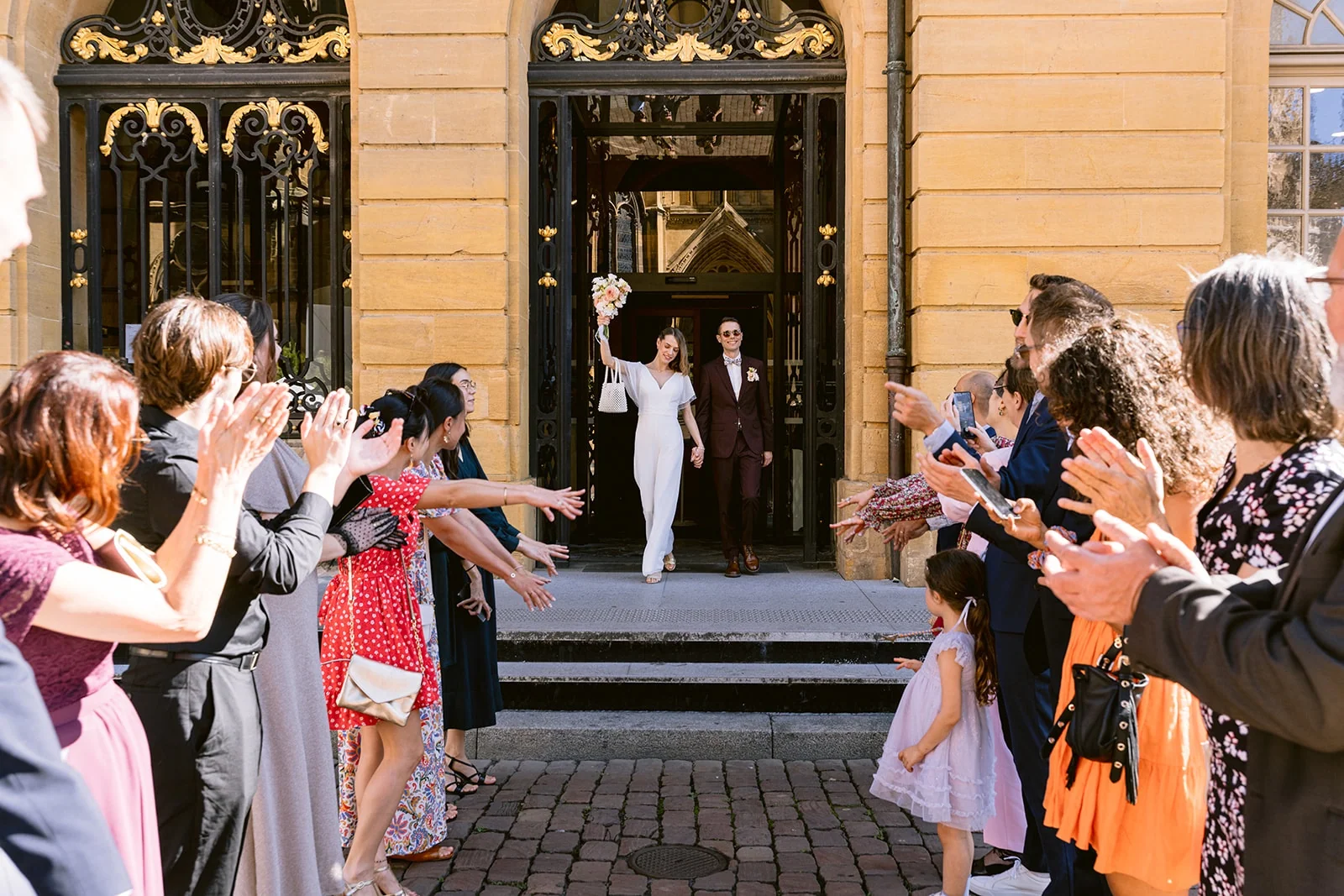 Les mariés sortent d’un bâtiment sous les applaudissements des invités alignés de chaque côté des marches.