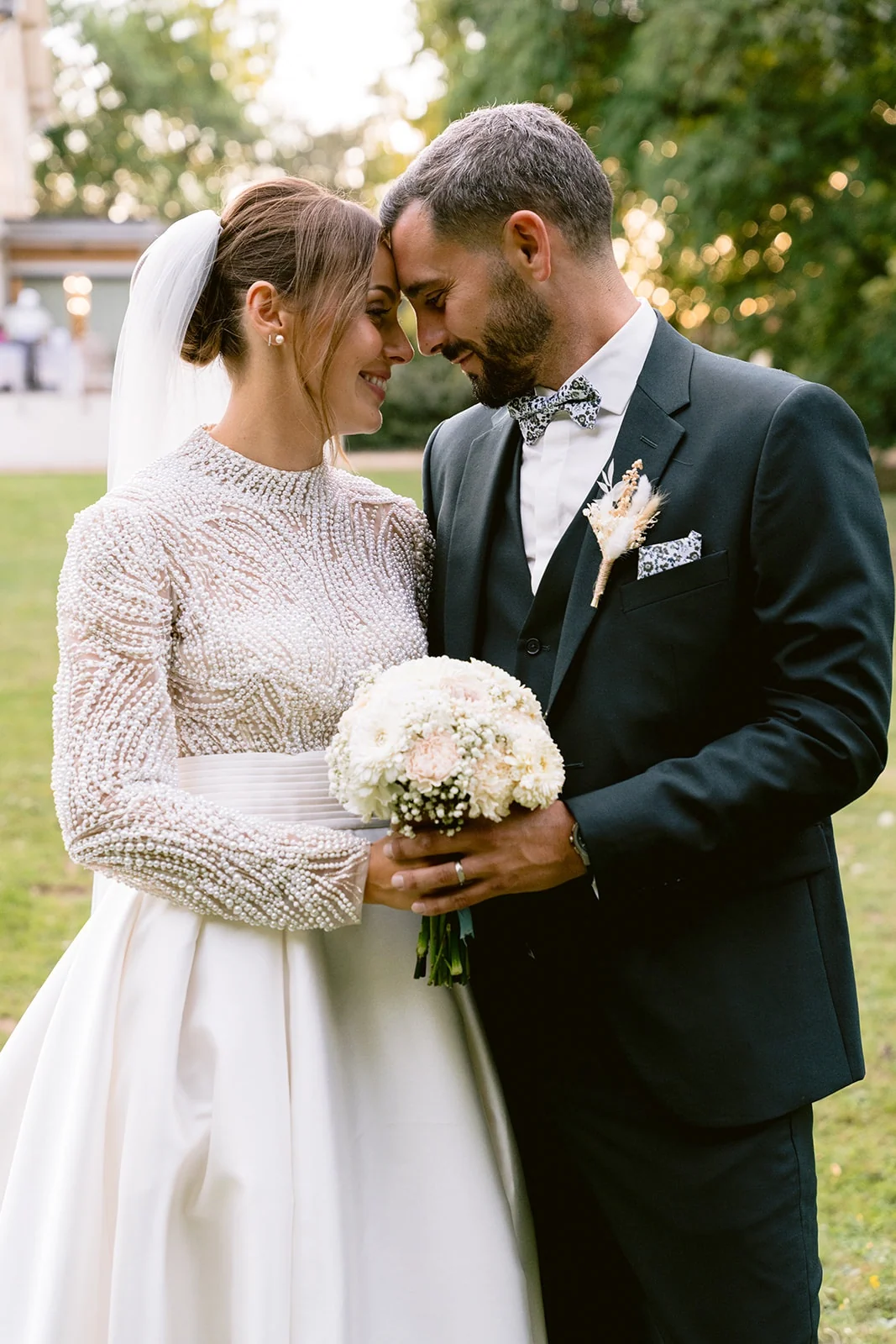 Les mariés rapprochent leurs fronts au-dessus du bouquet de fleurs claires.