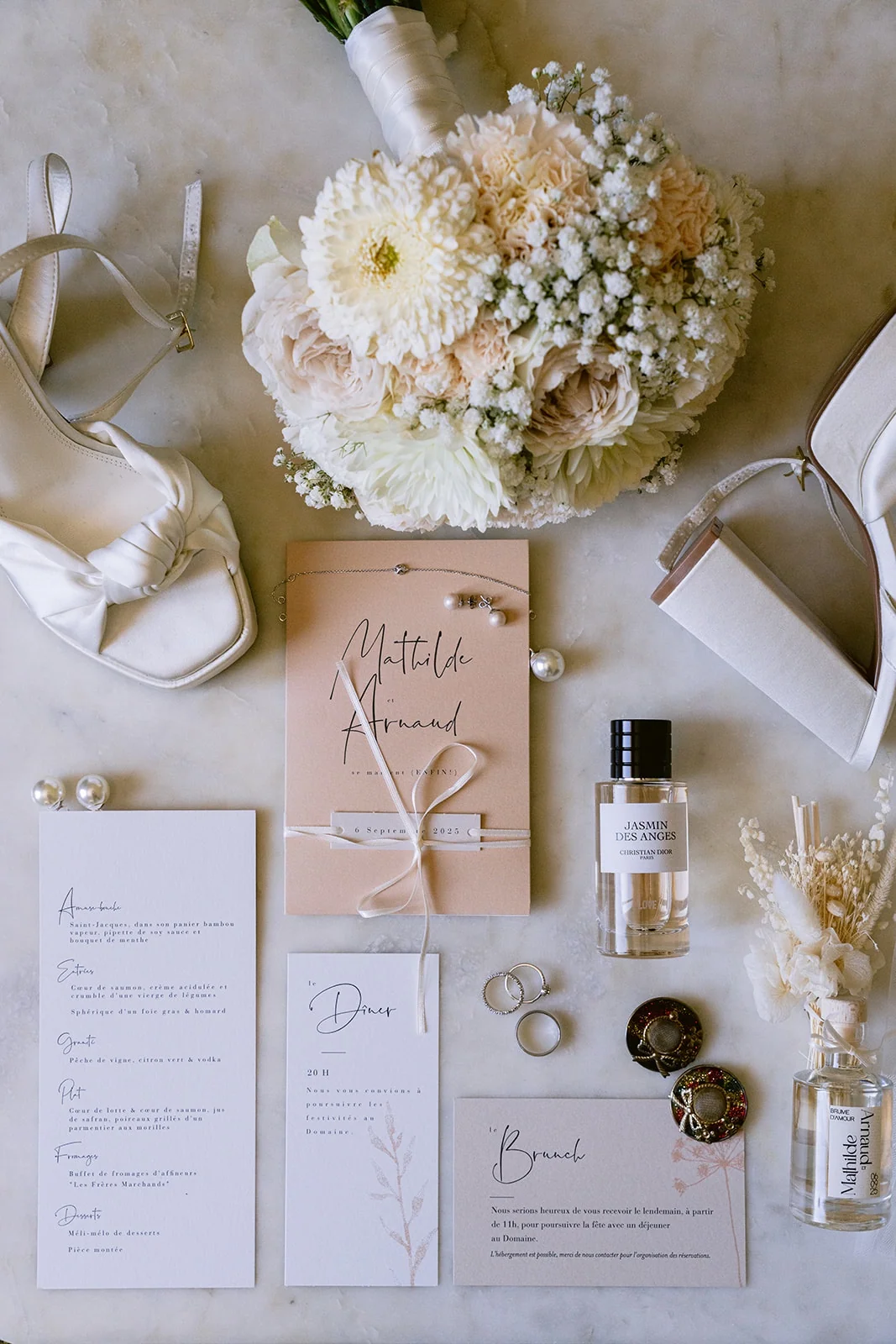 Le bouquet, les alliances, le parfum et la papeterie du mariage sont réunis sur un tissu clair.