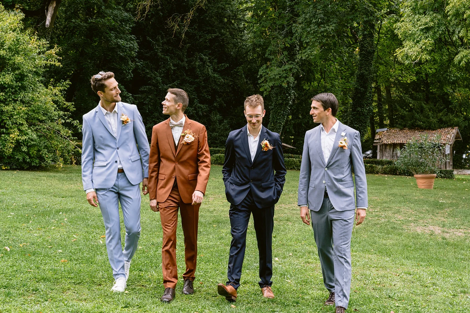 Le marié en costume brun marche sur la pelouse avec trois hommes en costume.