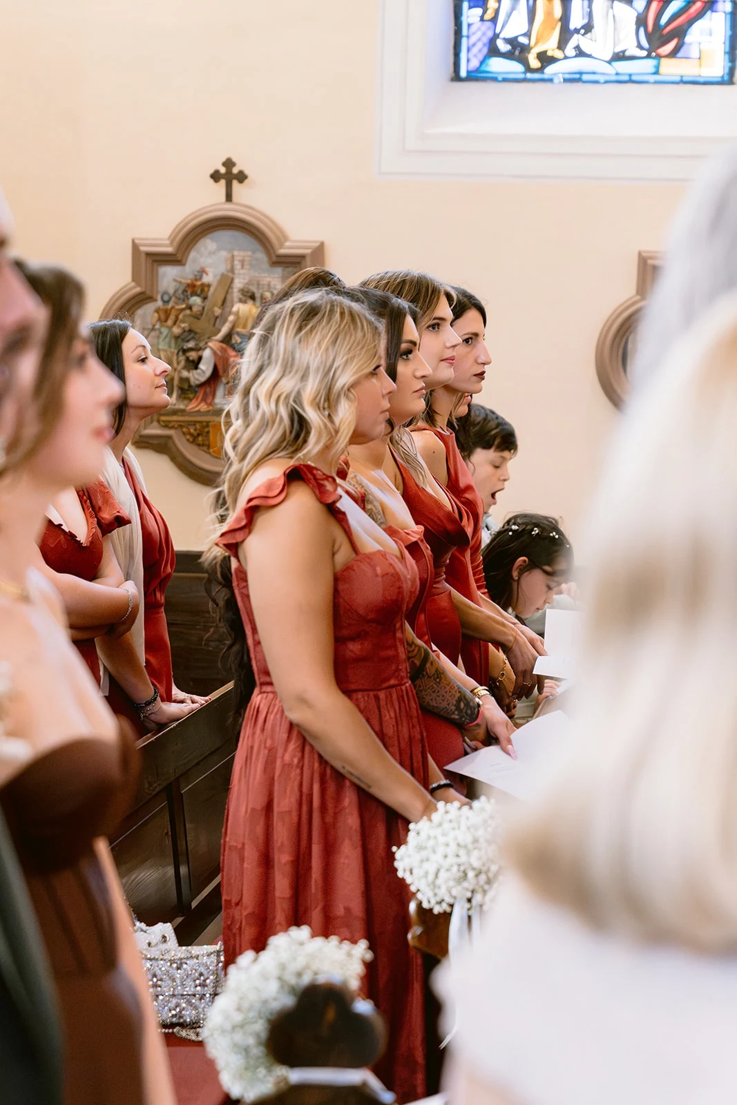 Des invitées en robes aux tons rouges se tiennent debout dans les bancs de l’église.