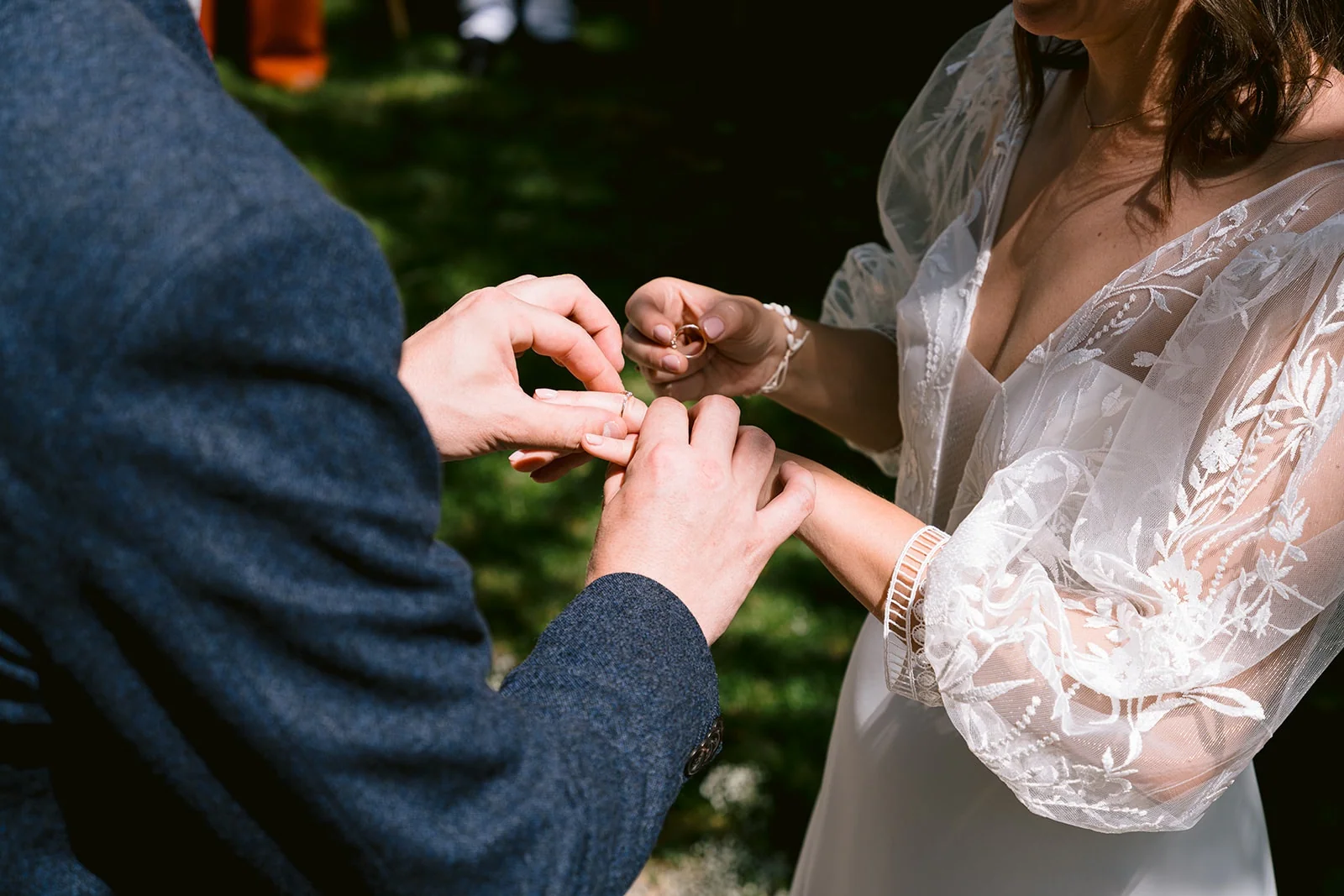 Gros plan sur le marié qui glisse une alliance au doigt de la mariée, tandis qu’elle tient une seconde bague.