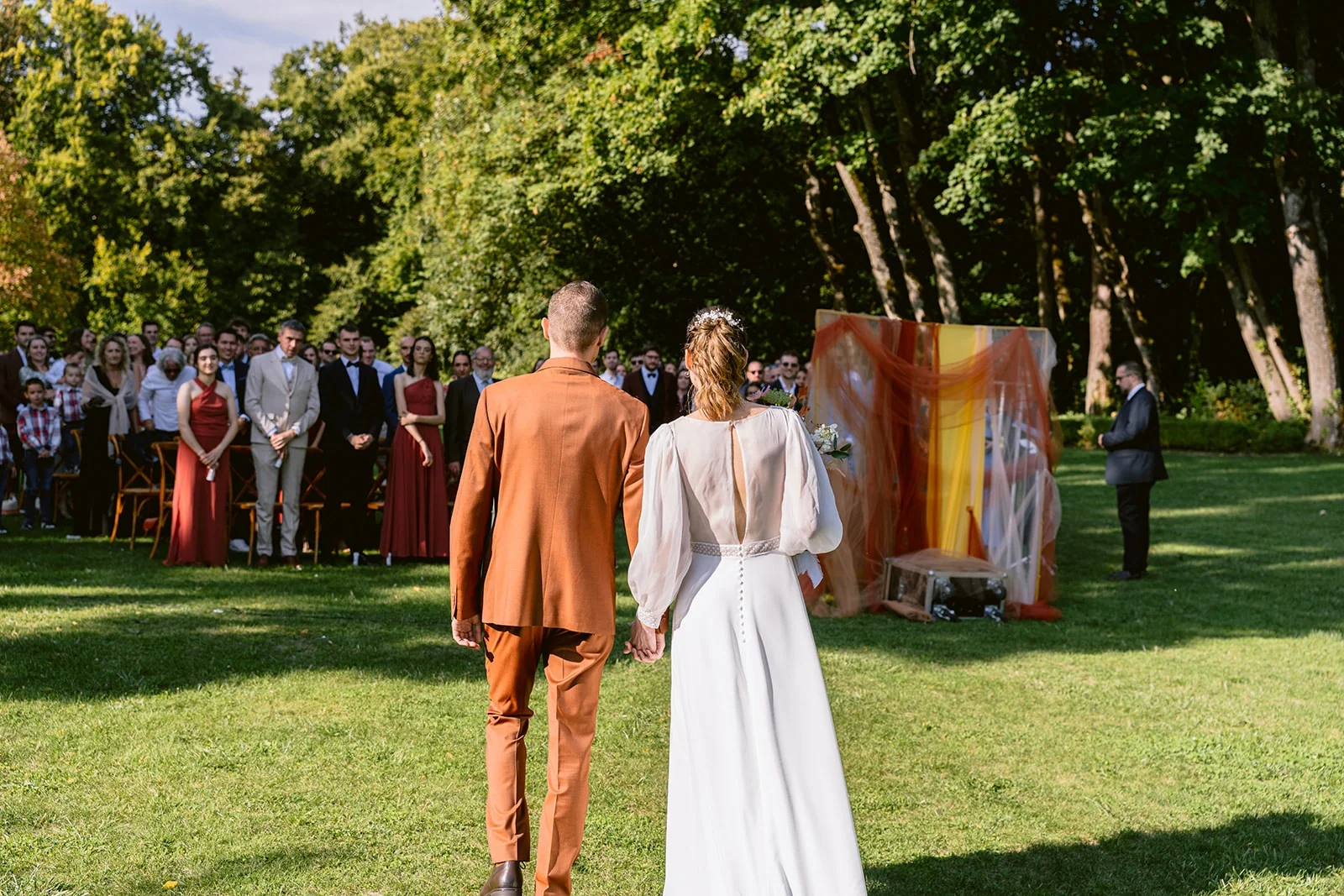 Vus de dos, les mariés se tiennent la main et avancent vers les invités réunis pour la cérémonie.