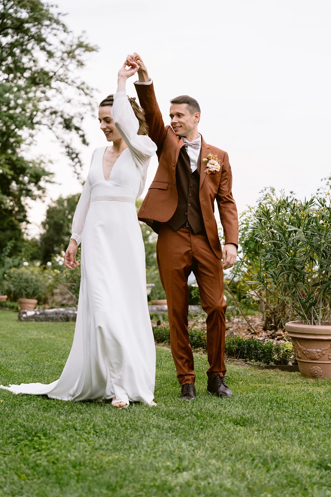 Le marié lève leurs mains jointes pour faire tourner la mariée dans le jardin.