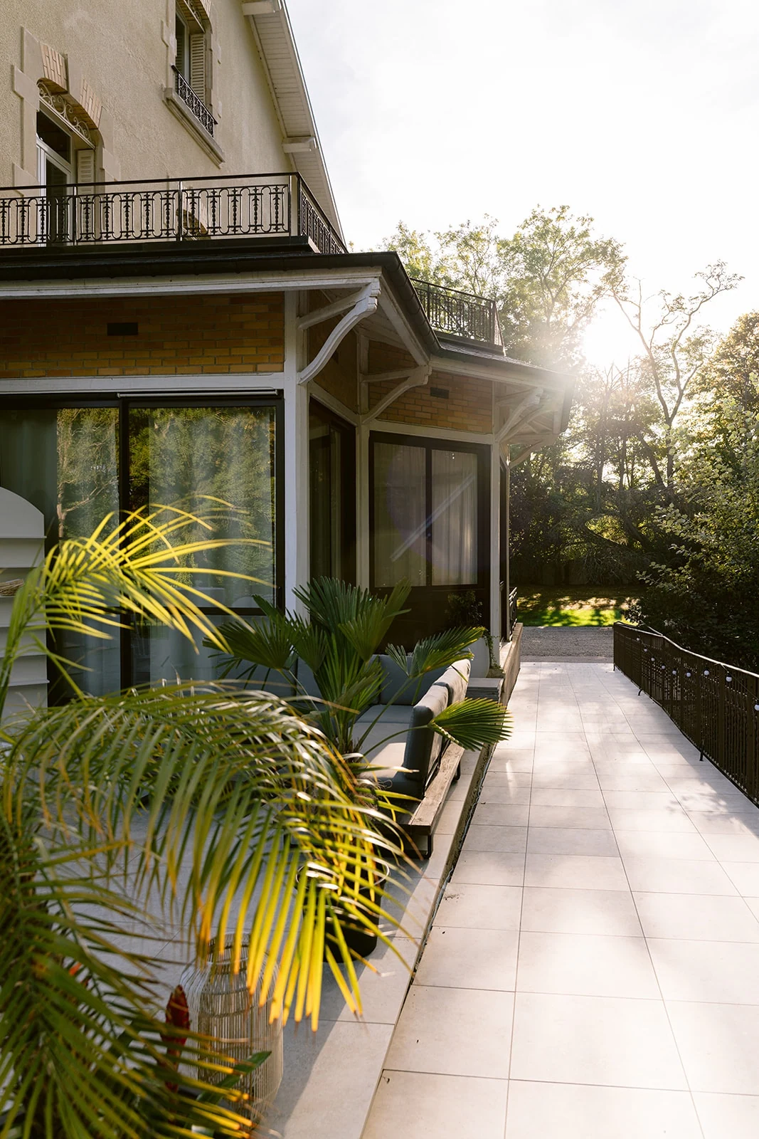 Le soleil éclaire la terrasse et la véranda du domaine, bordées de plantes.