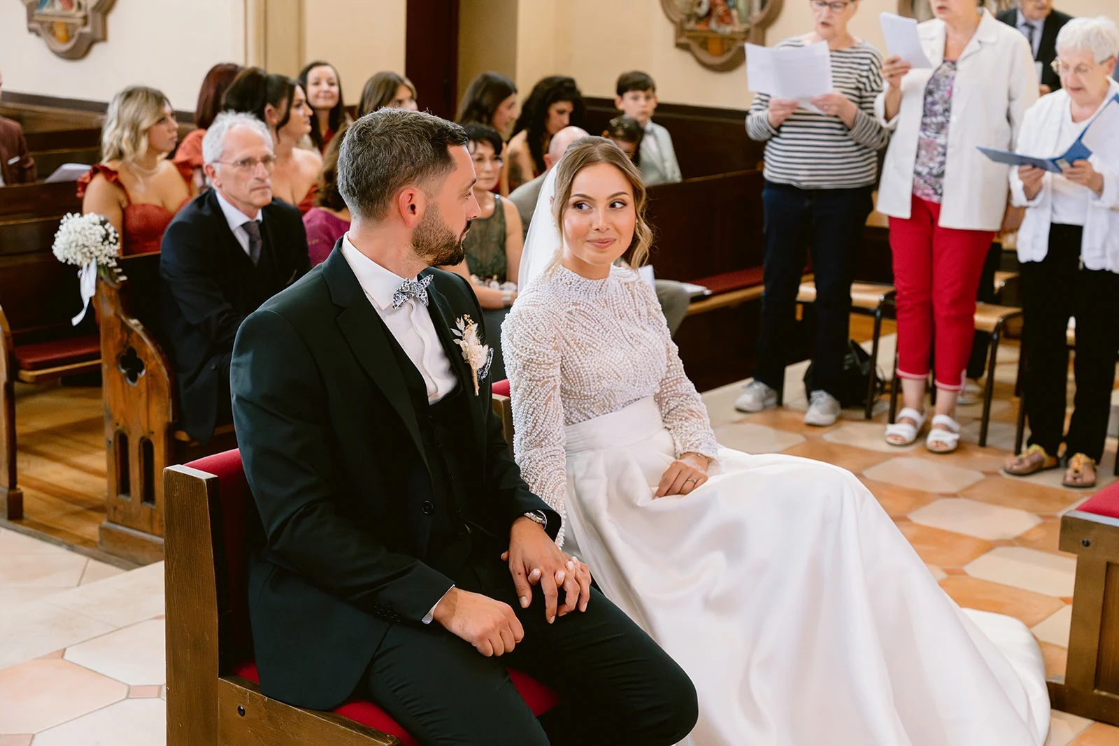 Les mariés, assis côte à côte dans l’église, échangent un regard.
