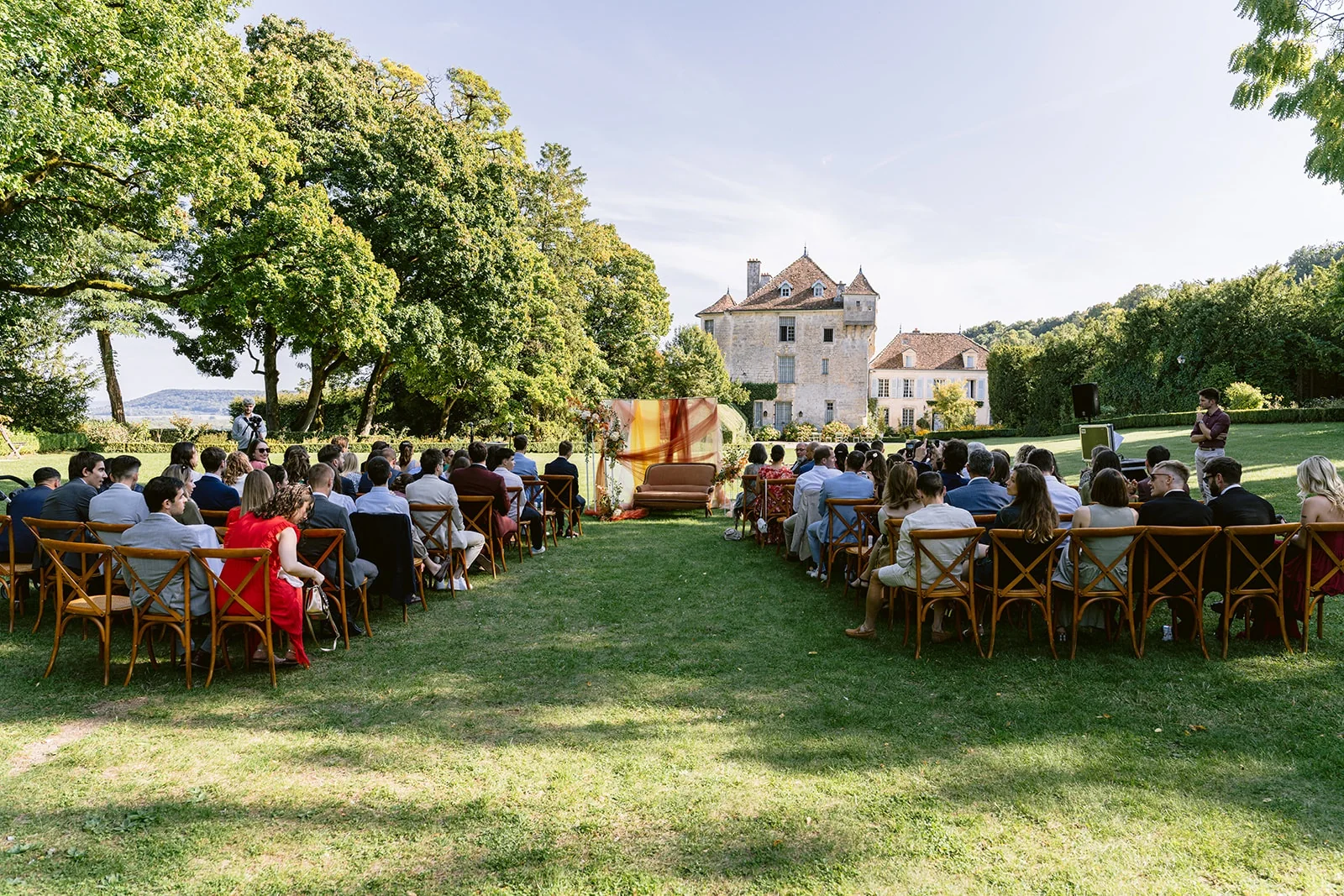 Les invités sont assis de part et d’autre d’une allée sur la pelouse, face au décor de cérémonie.