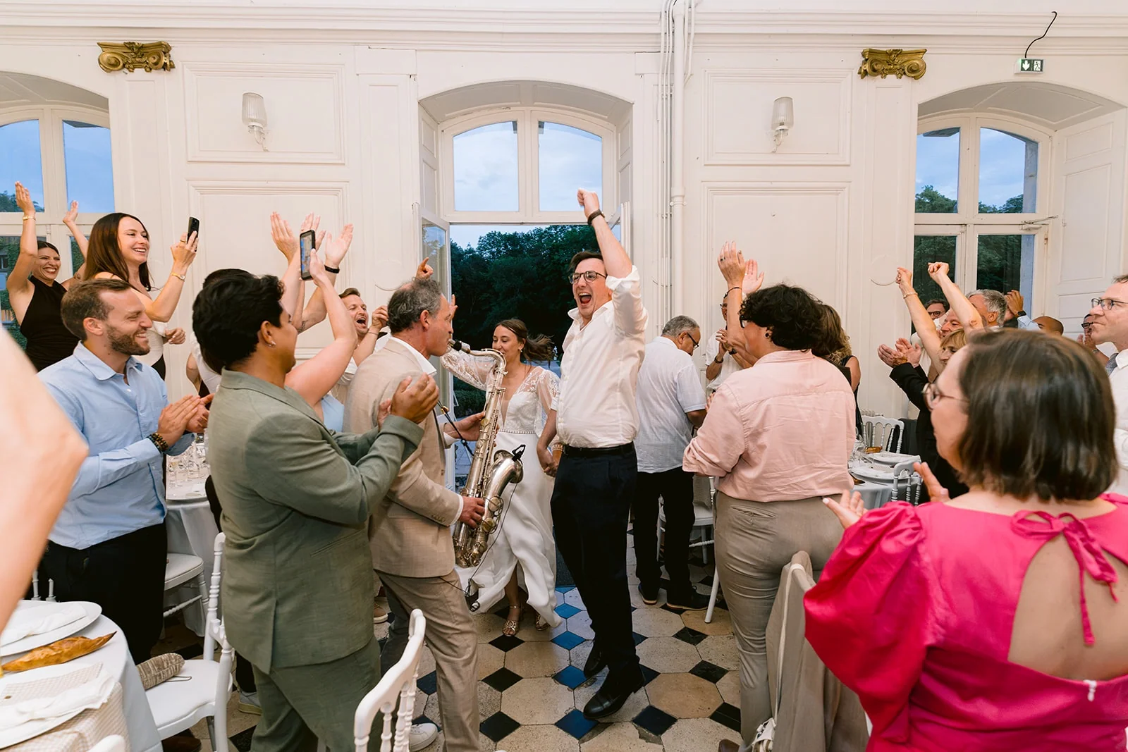 Des invités applaudissent et lèvent les bras dans une salle de réception au sol à damier.
