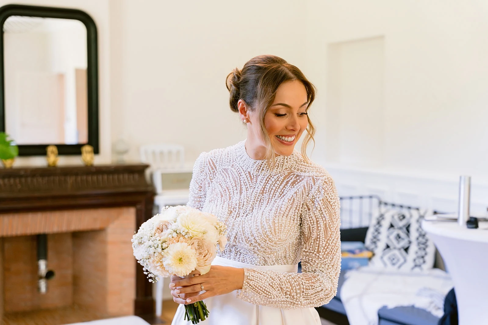 La mariée sourit en tenant son bouquet de fleurs claires.