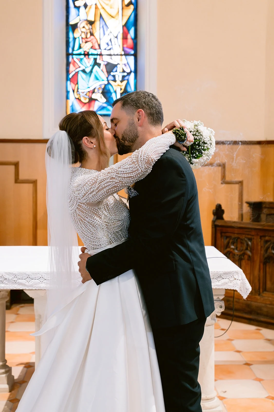 Les mariés s’embrassent devant les vitraux de l’église.