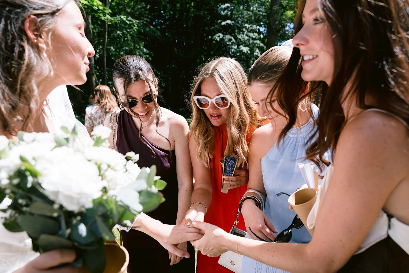 Plusieurs invitées se penchent pour regarder la main de la mariée, qui tient son bouquet blanc de l’autre main.