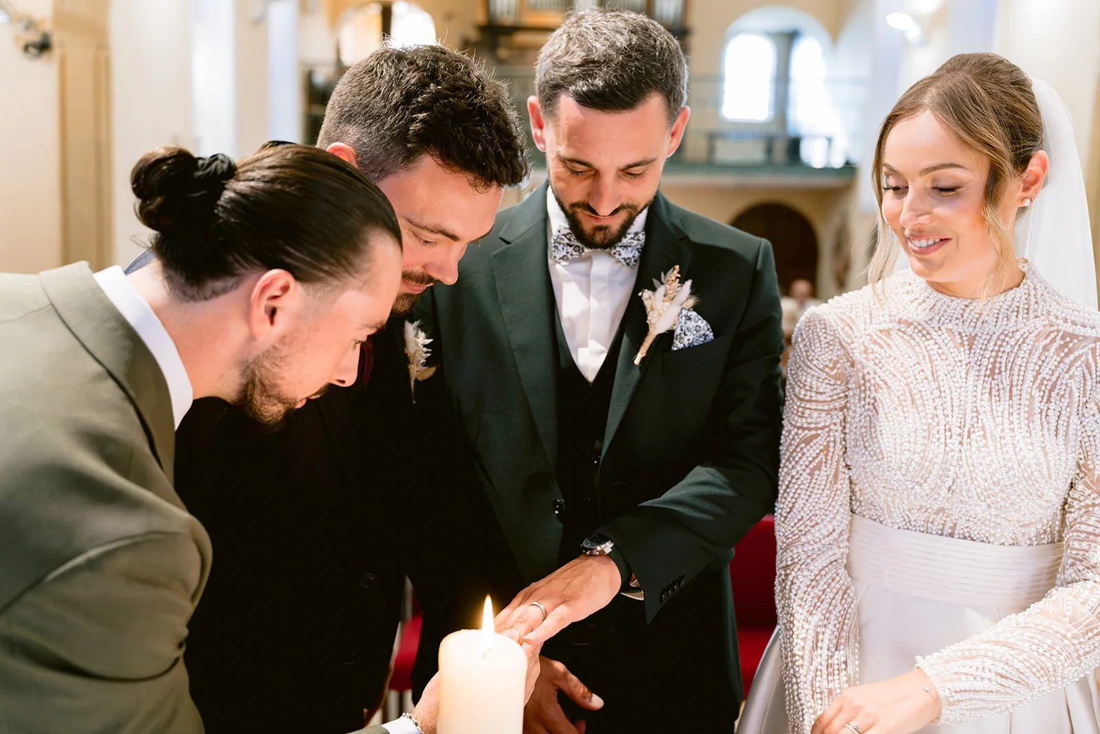 Les mariés et leurs proches réunissent leurs mains autour d’une bougie dans l’église.
