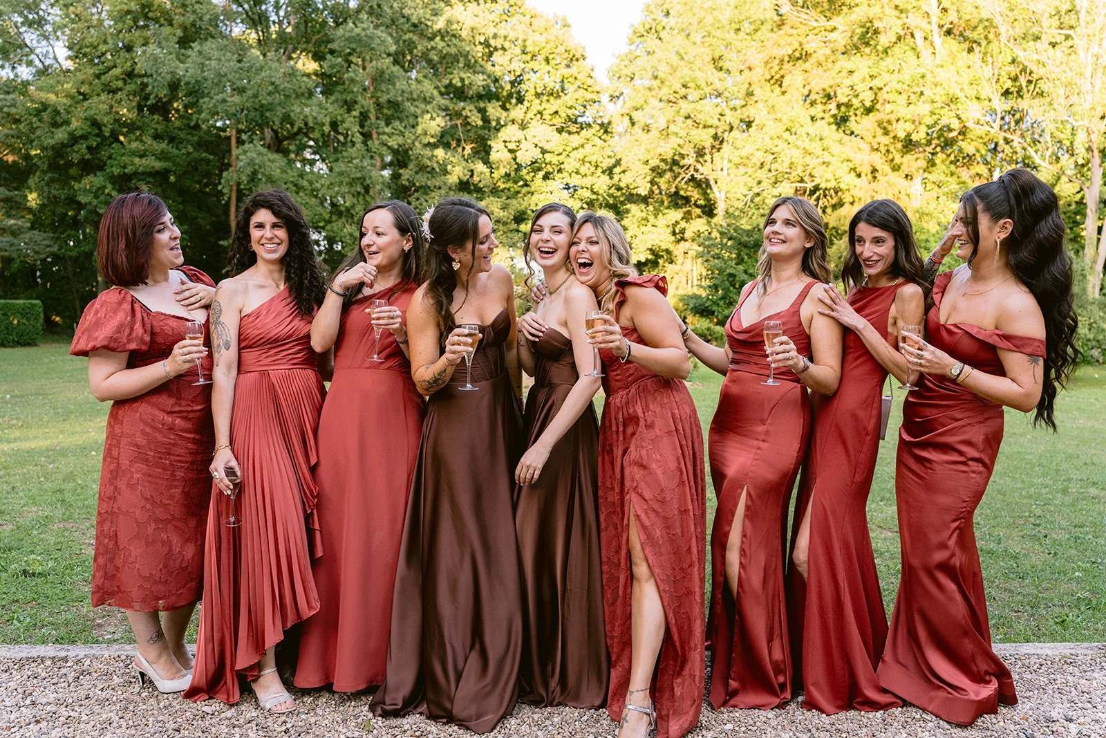 Un groupe d’invitées en robes aux tons chauds rit et trinque dans le jardin.