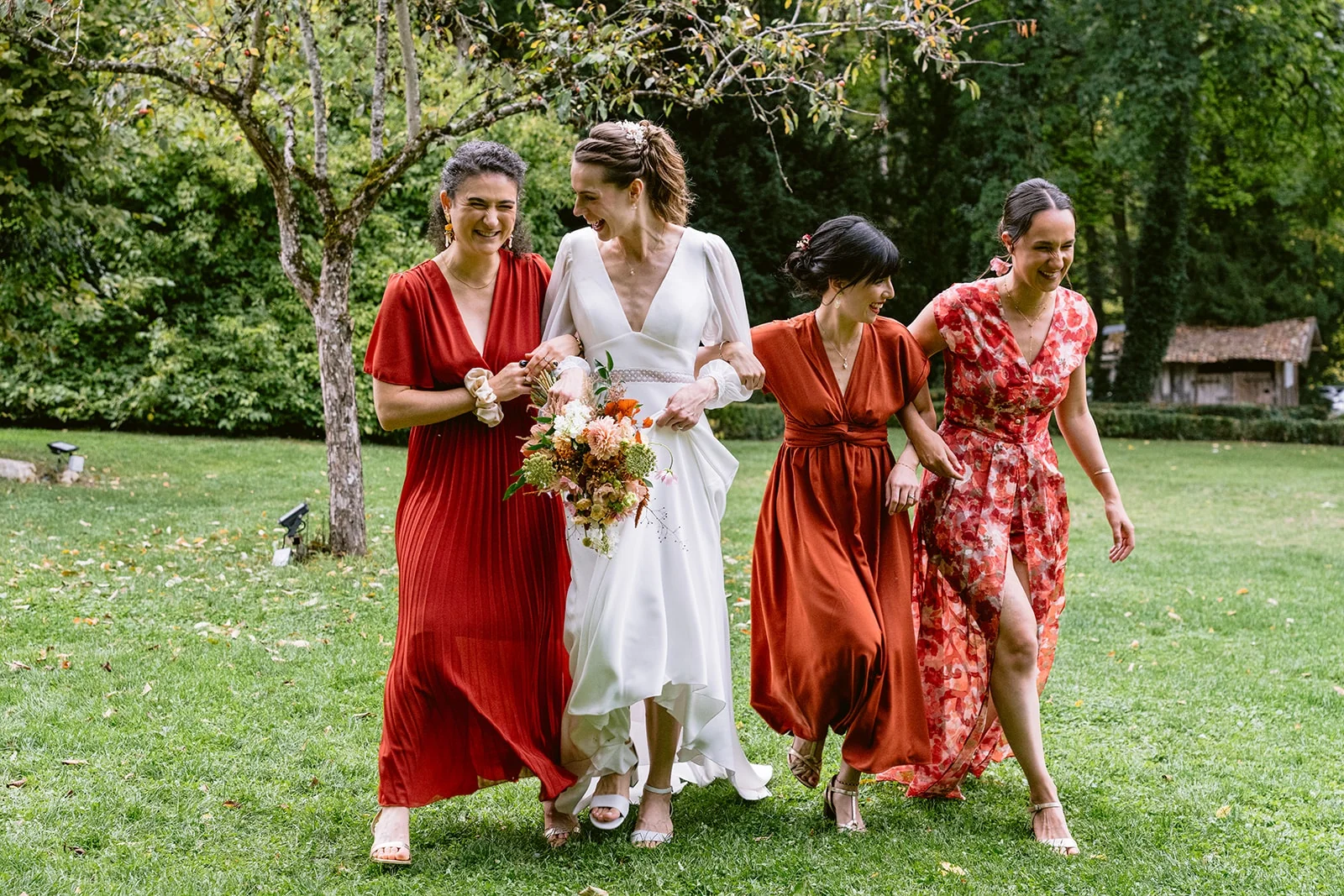 La mariée marche sur la pelouse avec trois femmes en robes rouges, son bouquet à la main.