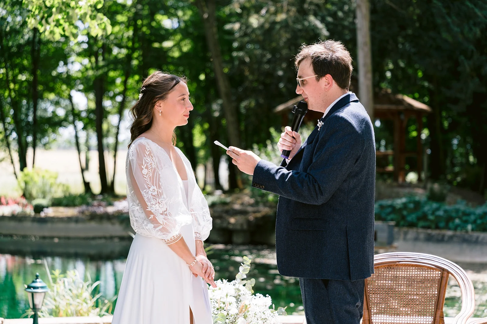 Le marié lit un texte au microphone face à la mariée pendant la cérémonie en plein air.