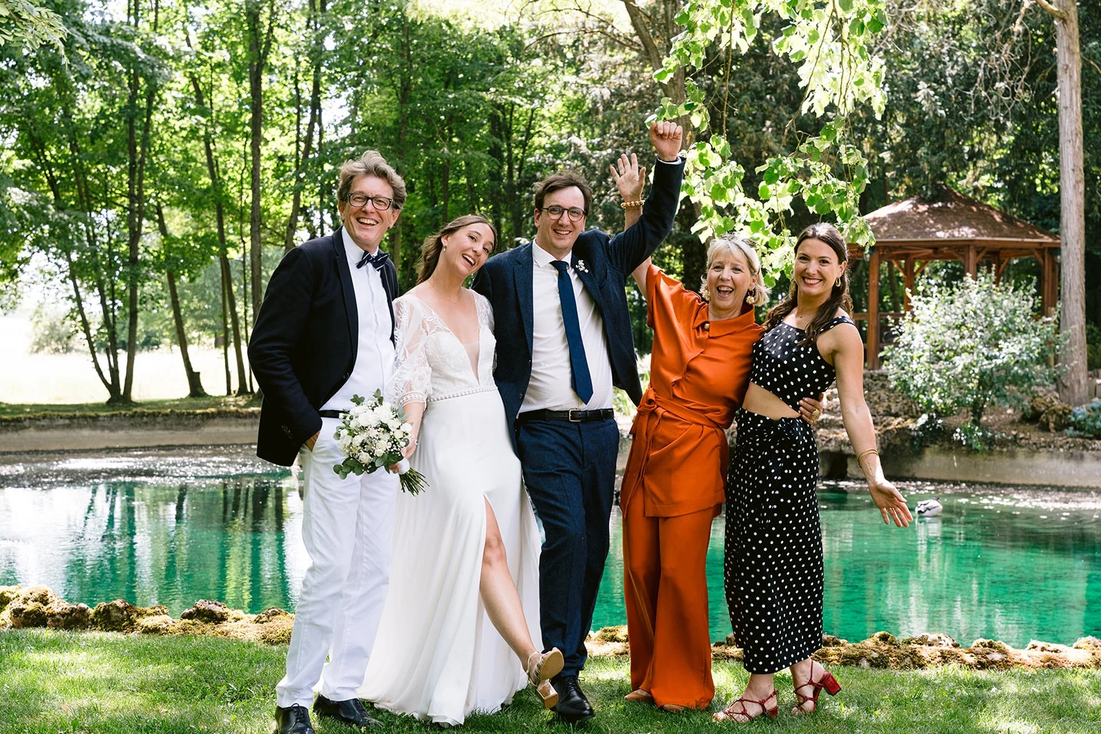 Les mariés posent avec trois invités devant un bassin turquoise, tous souriants, certains levant les bras.