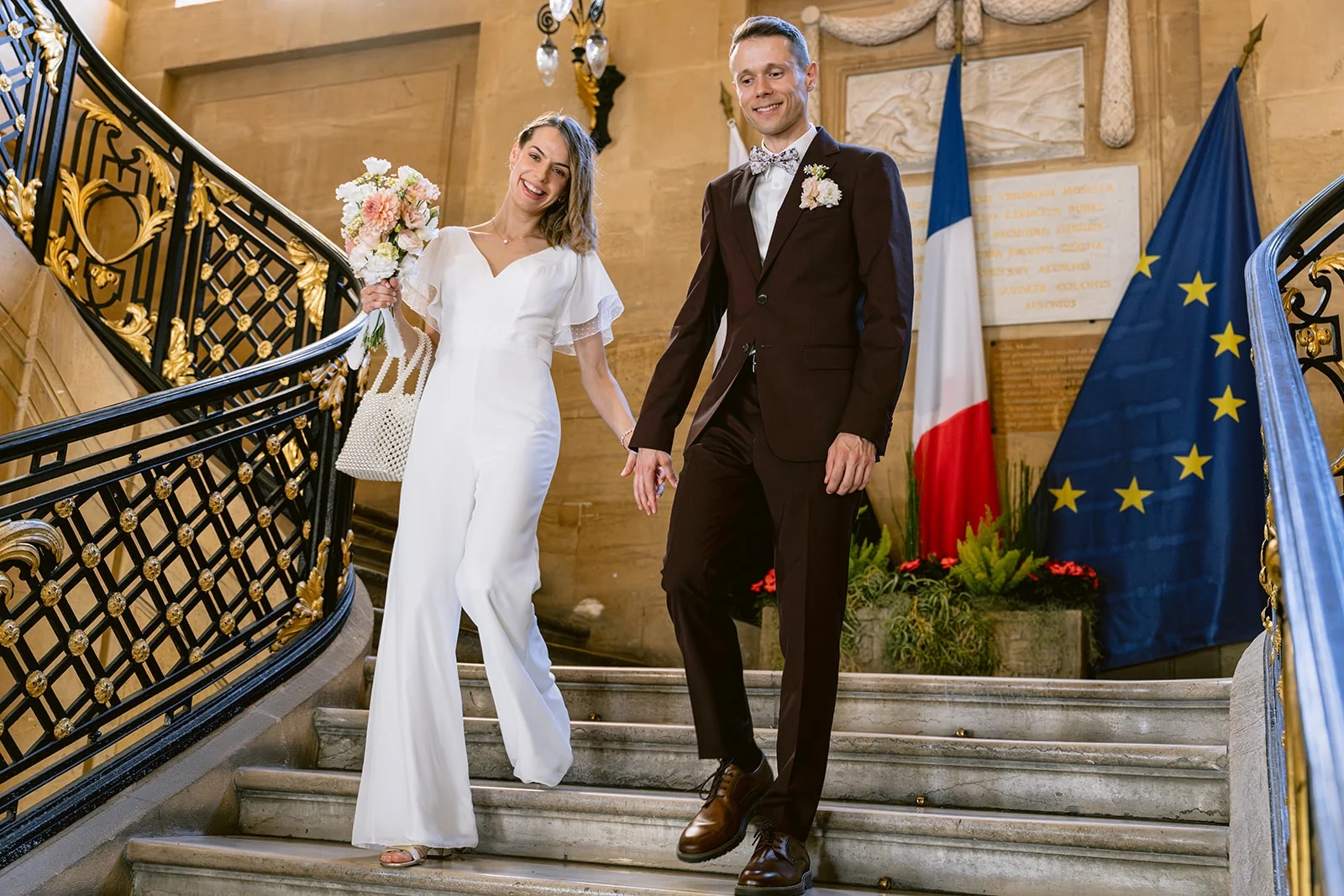 Les mariés se tiennent la main sur un escalier, devant les drapeaux français et européen.