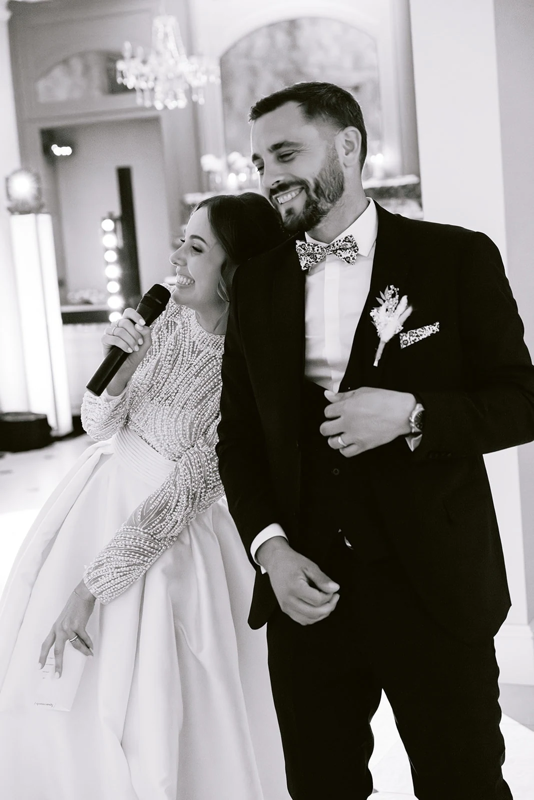 En noir et blanc, la mariée prend la parole au micro aux côtés du marié.