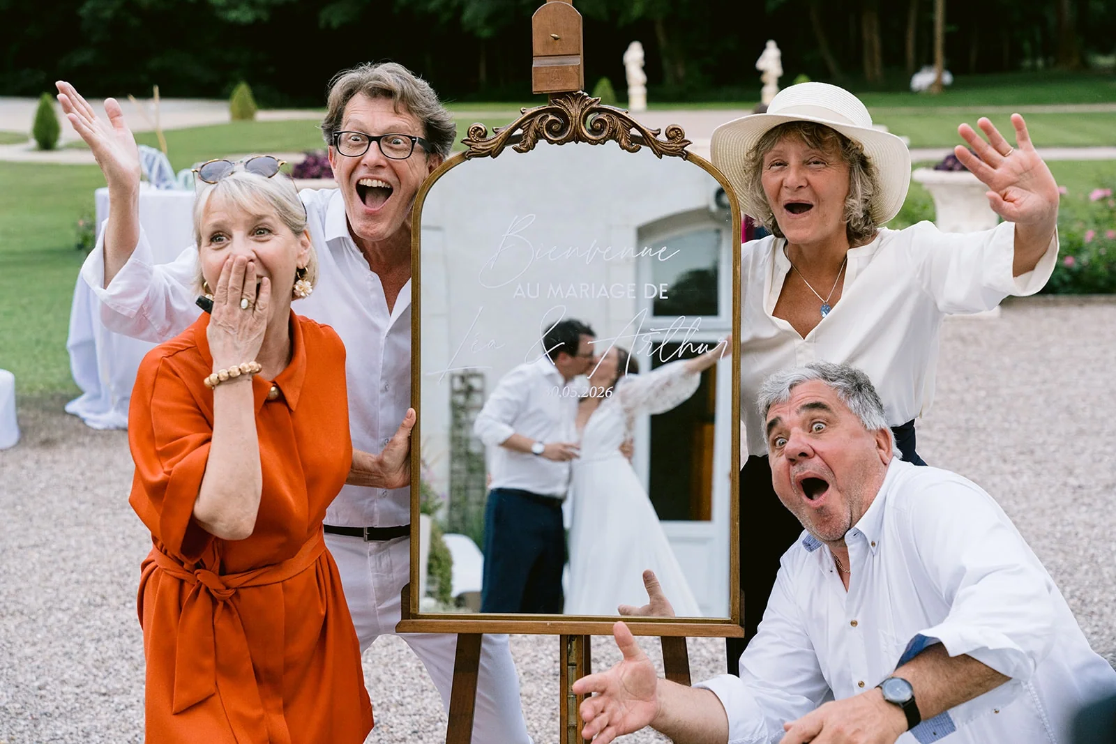 Quatre invités prennent des poses amusées autour d’un miroir doré où se reflètent les mariés.