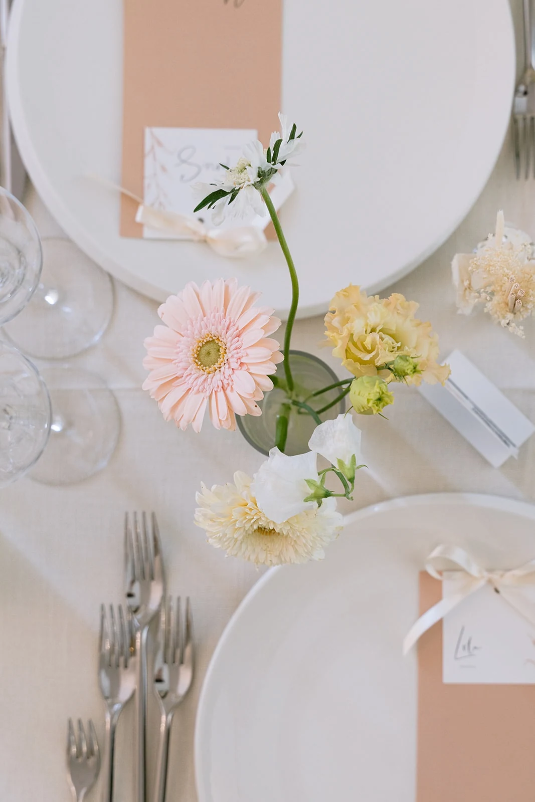 Des fleurs blanches, jaunes et roses décorent une table dressée dans des tons pastel.