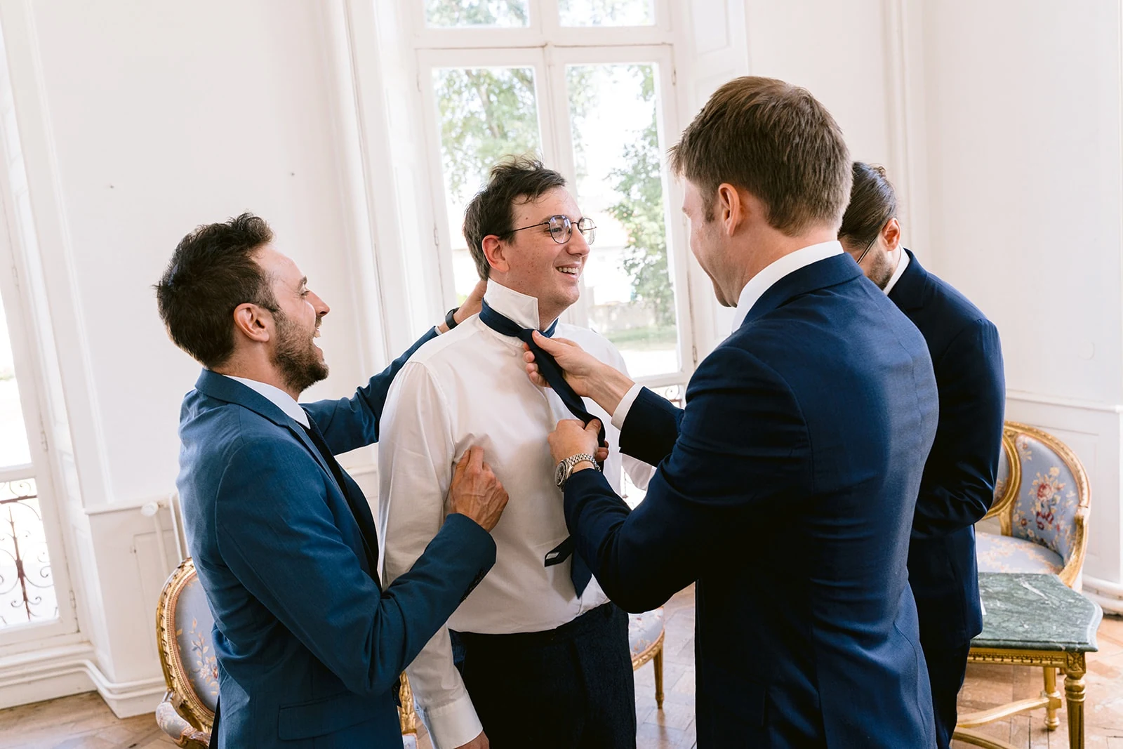 Les proches du marié ajustent sa cravate et ses bretelles en souriant.