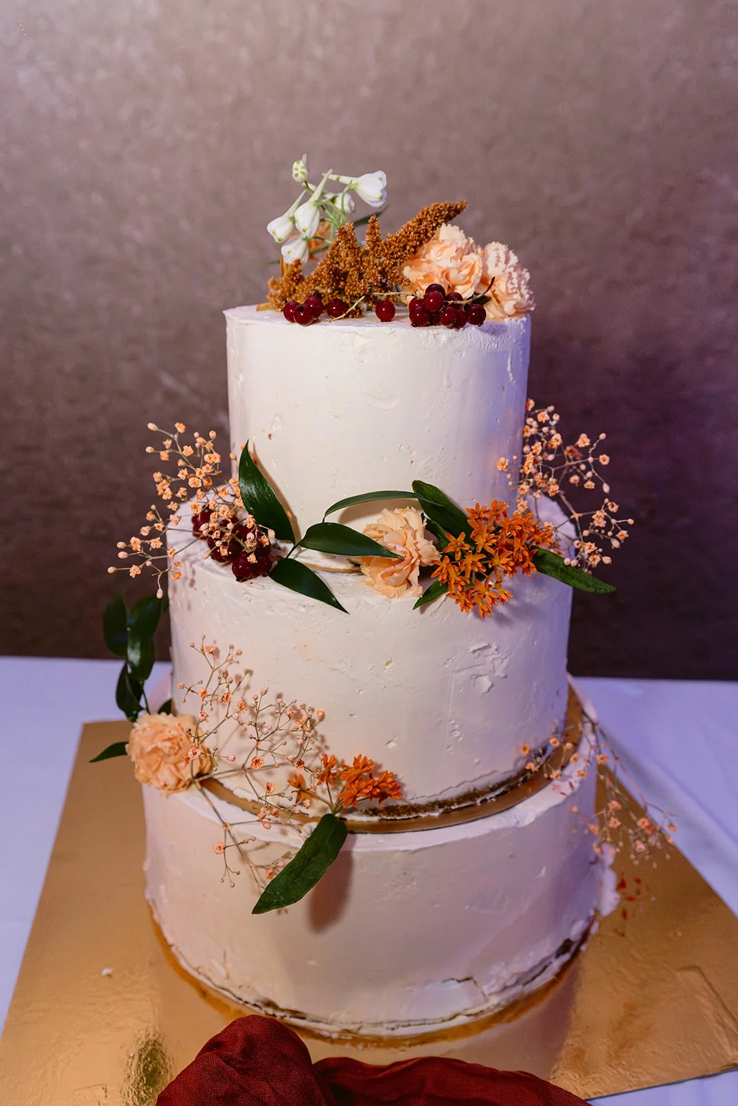 Un gâteau blanc à trois étages est décoré de fleurs, de feuillages et de touches dorées.