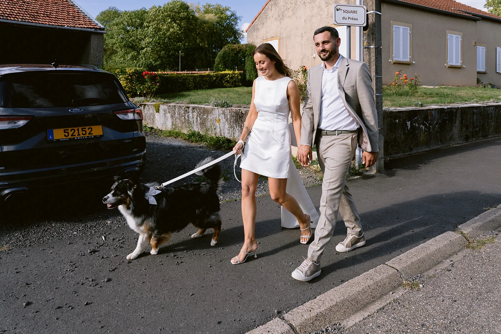 Les mariés marchent main dans la main dans la rue, accompagnés de leurs chiens.
