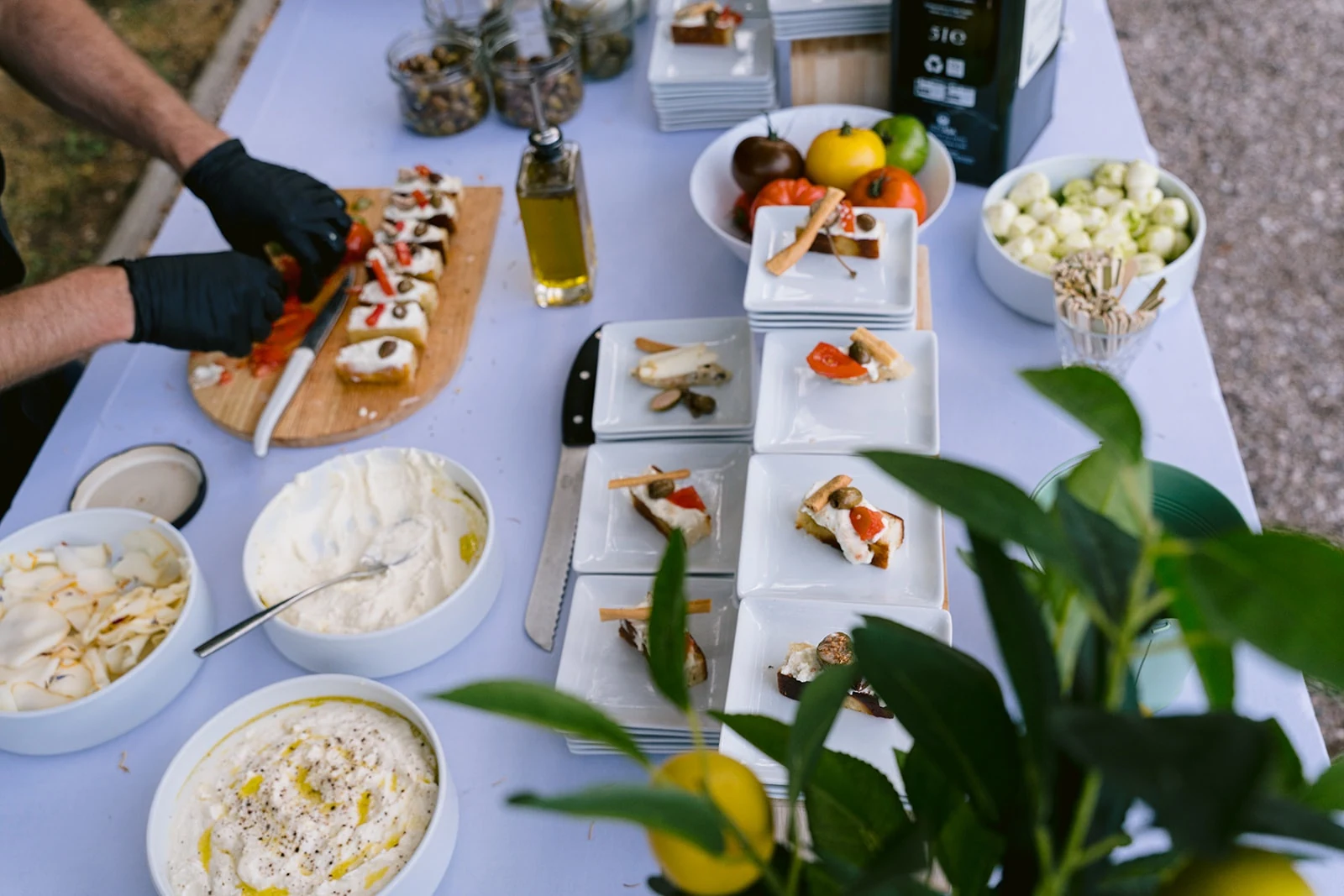 Vue de dessus d’un atelier culinaire où des mains gantées garnissent des bouchées sur une table couverte d’ingrédients.