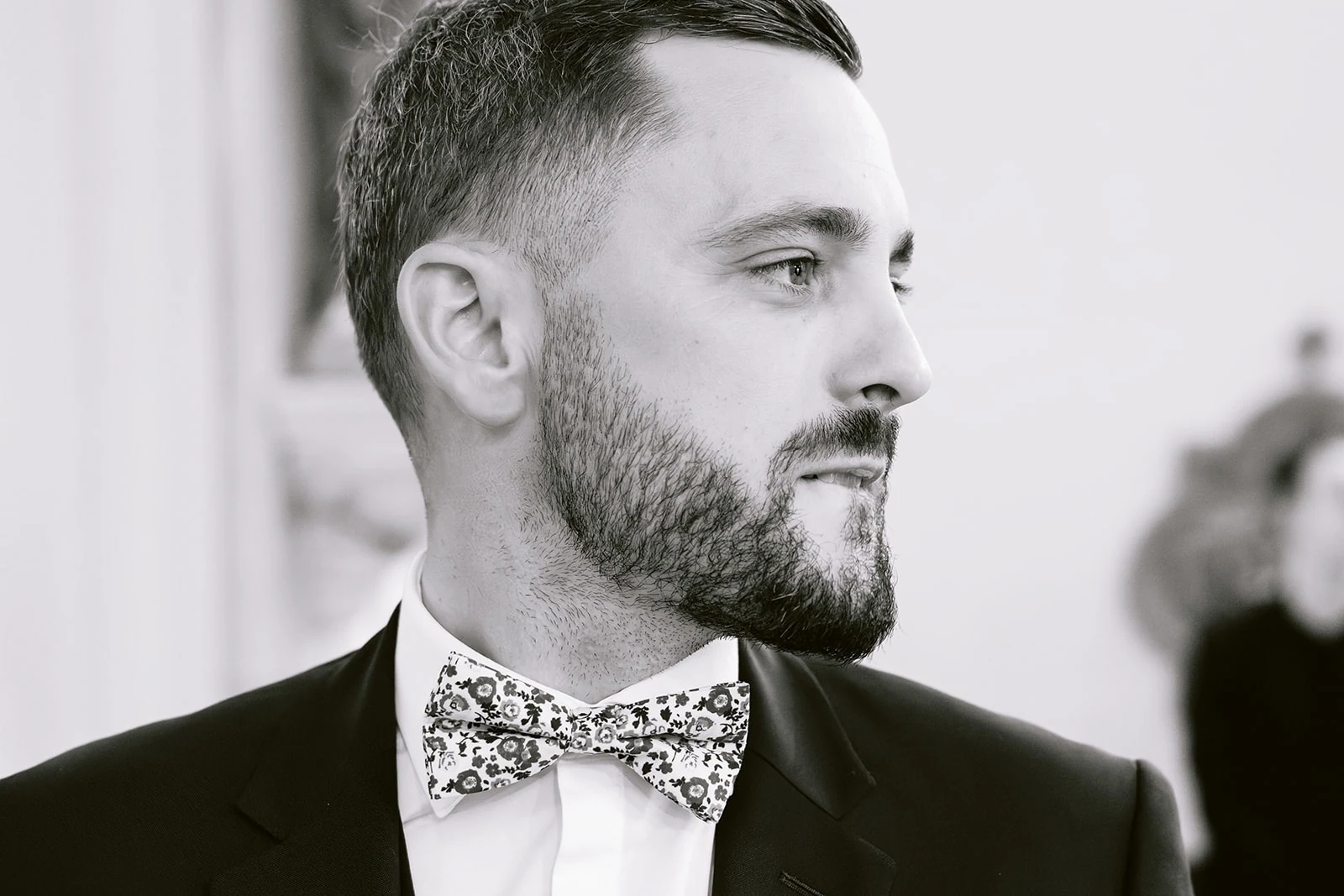 Portrait du marié en noir et blanc, portant un nœud papillon fleuri.