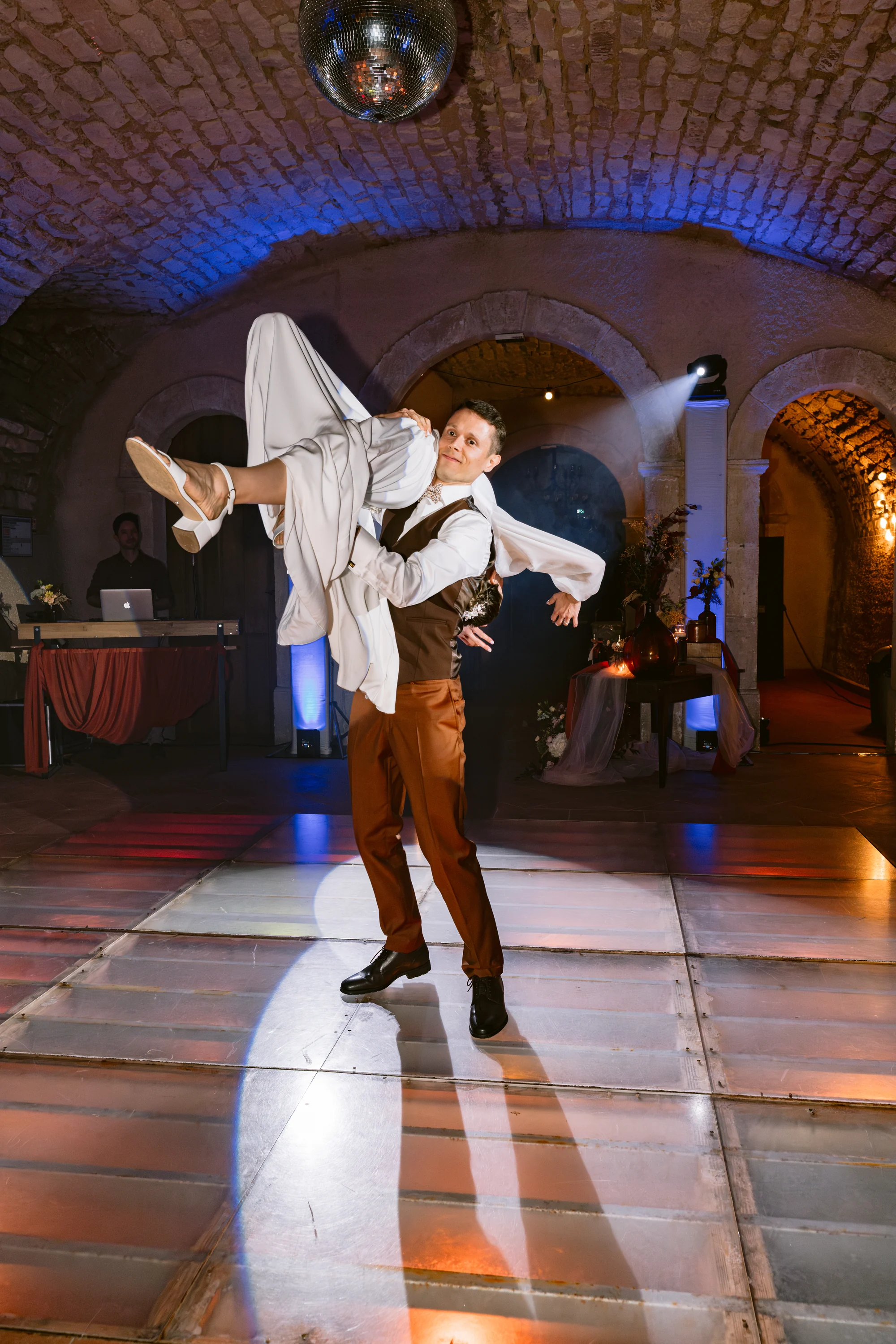 Le marié porte la mariée pendant une danse sous les voûtes en pierre.