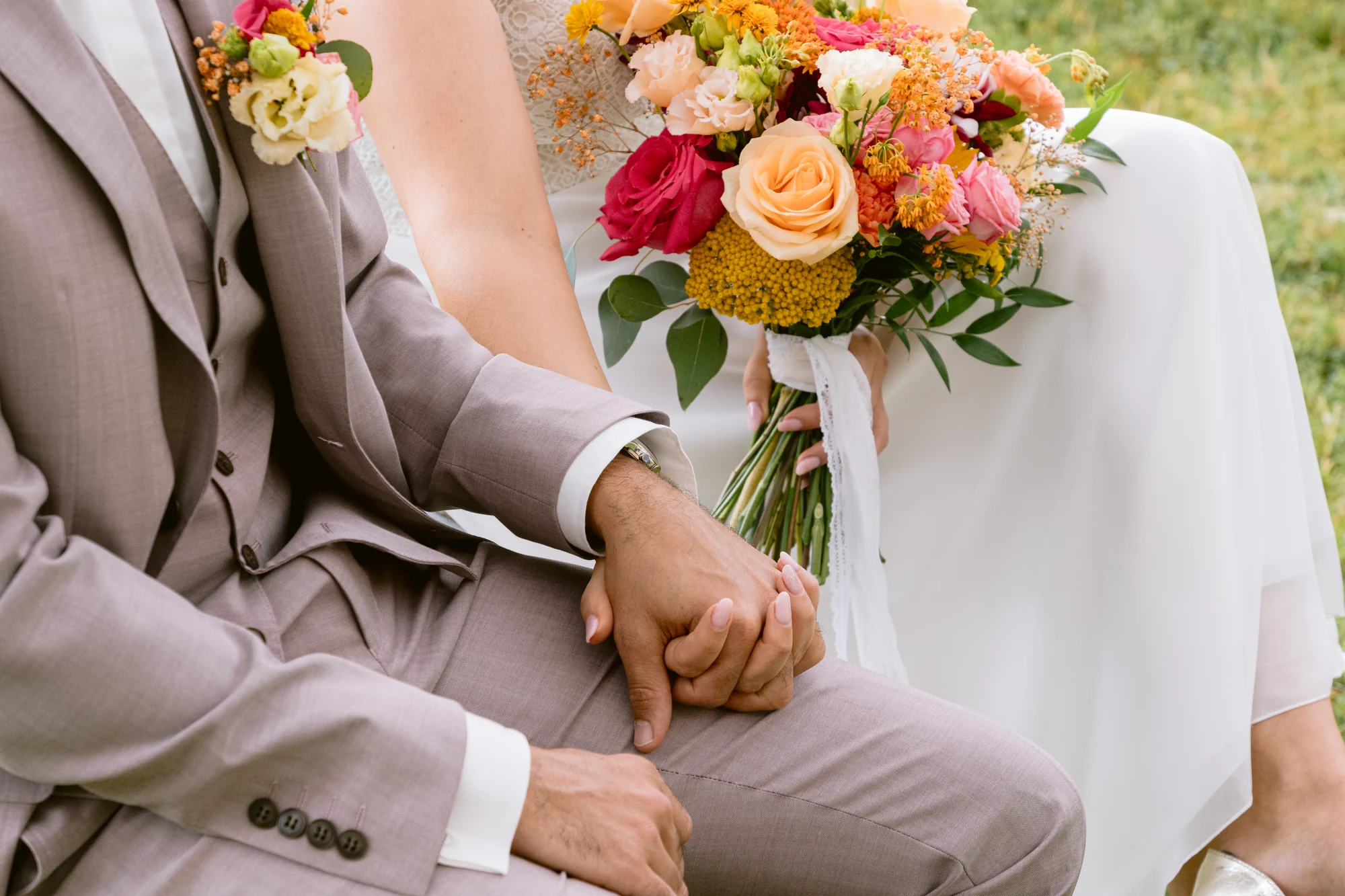 Les mains des mariés se rejoignent près d’un bouquet coloré.